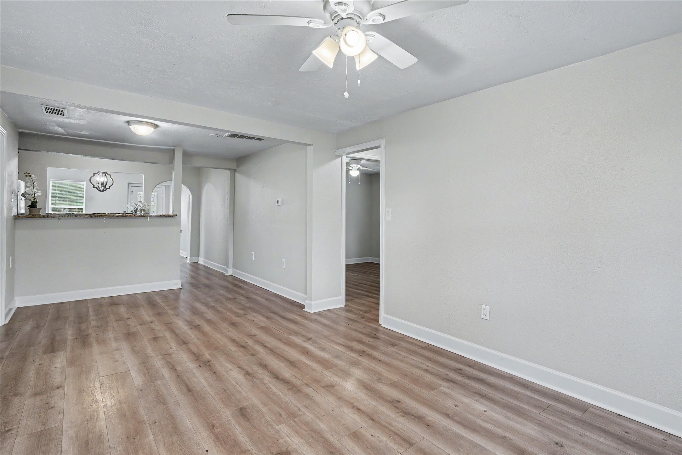 Spacious living area with wood-look flooring, fresh interior paint and a ceiling fan.