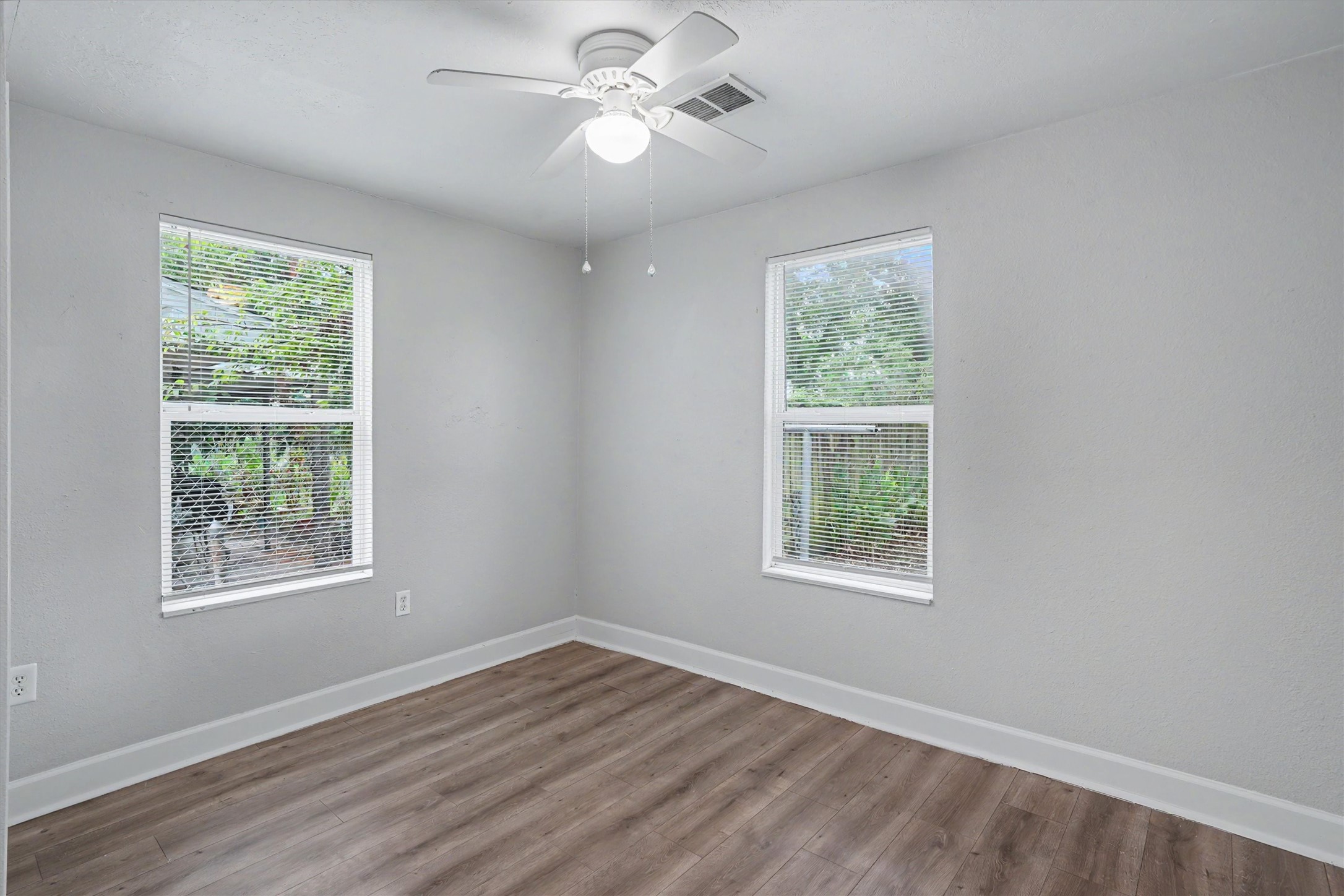 Bright third bedroom features two windows, ceiling fan and wood-look flooring.