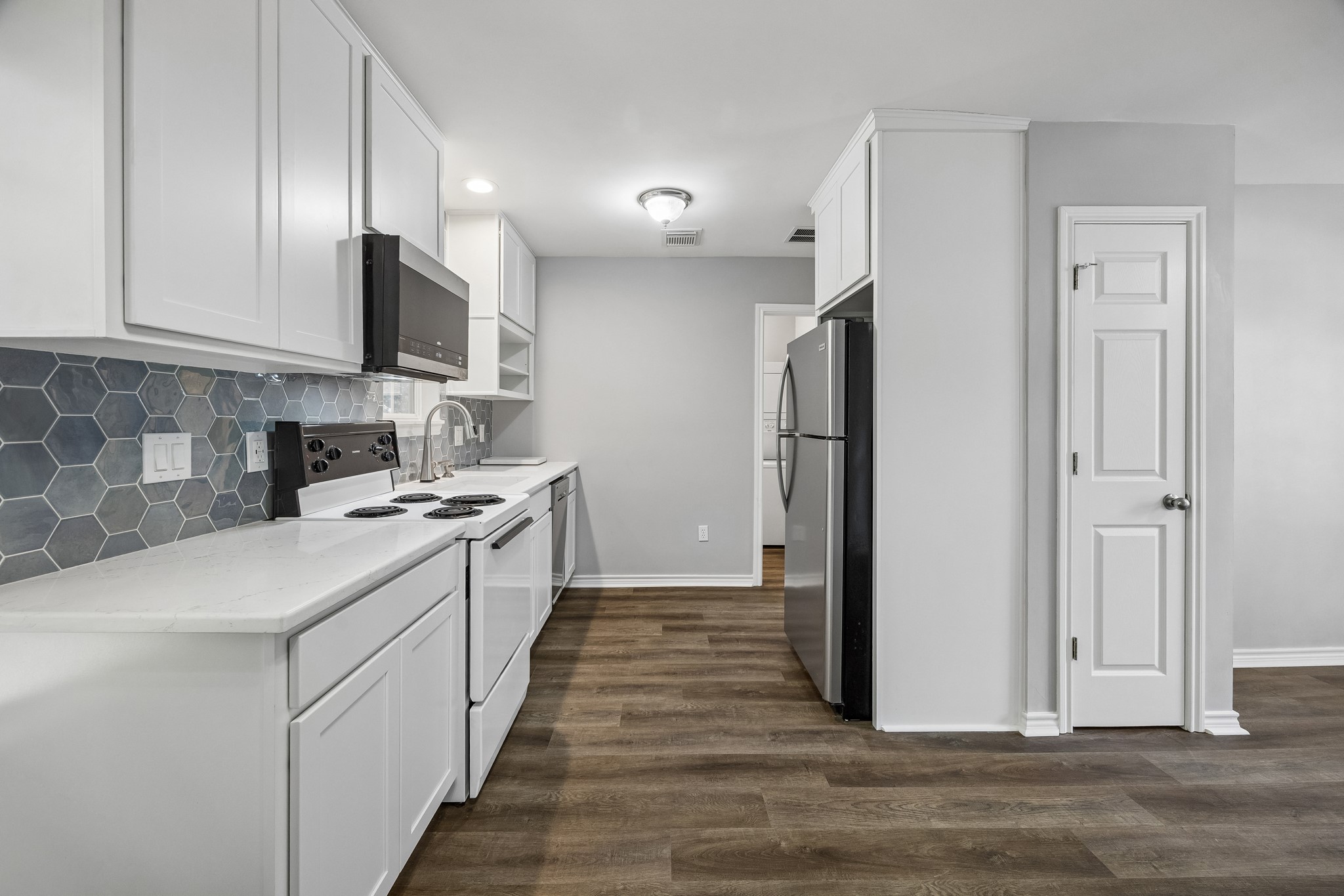 Garage apartment kitchen with white cabinetry, stainless steel appliances, and engineered wood flooring, offering a functional, well-appointed space for guests or extended stays.