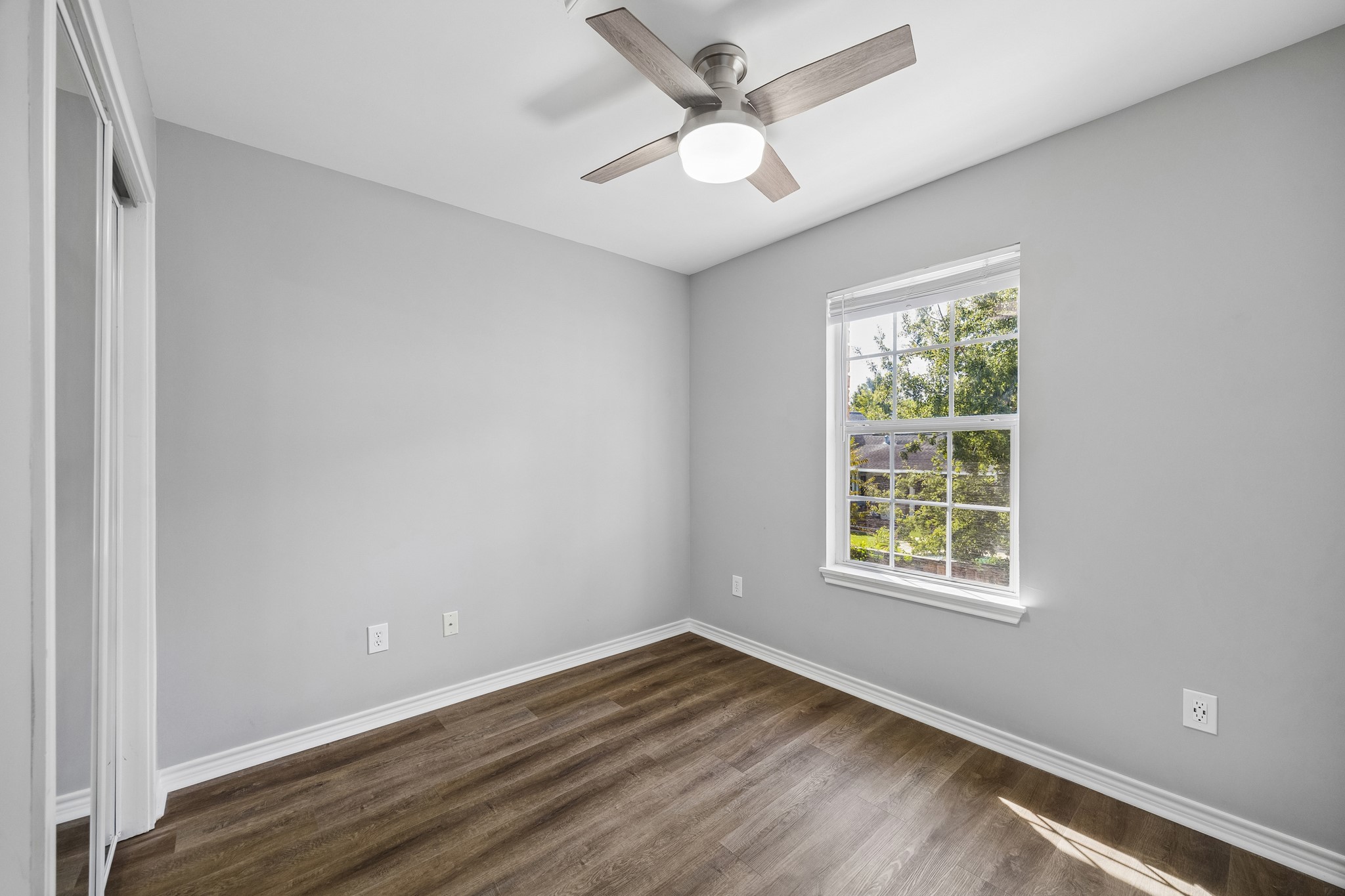 Garage apartment bedroom with engineered wood flooring, a ceiling fan, and natural light from a large window.