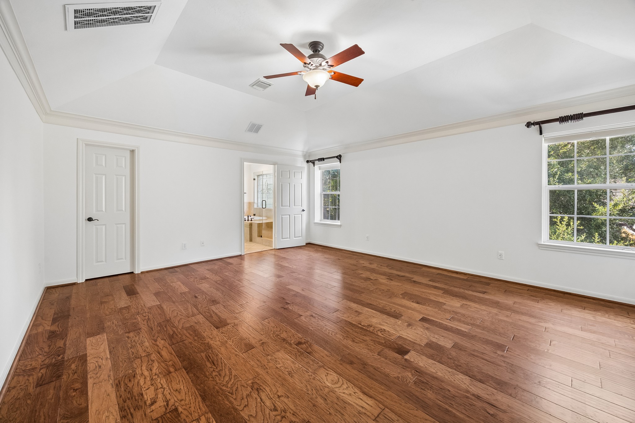 Spacious primary bedroom with rich hardwood floors, custom window treatments, and a ceiling fan, creating a comfortable and inviting retreat.