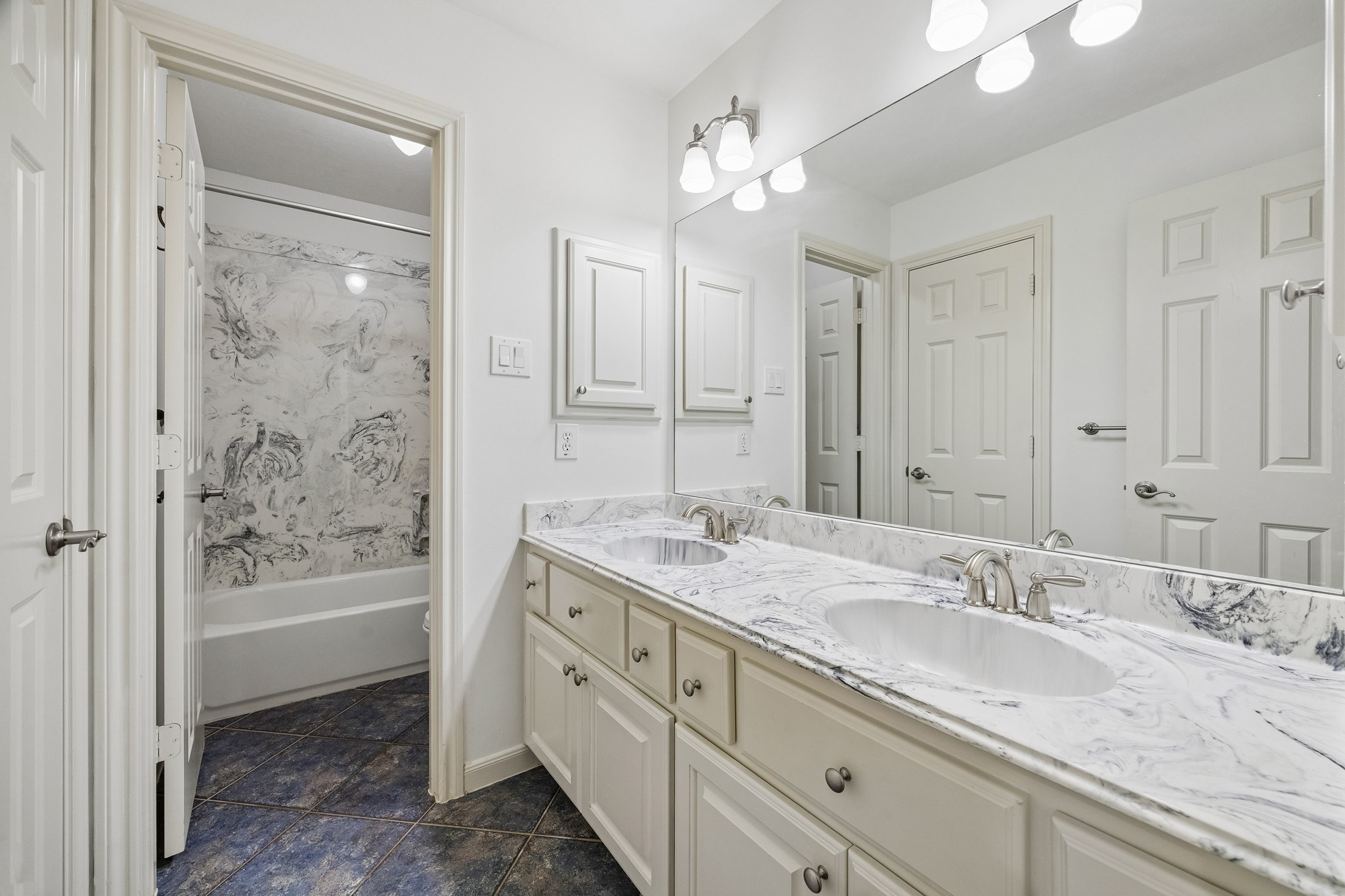 En suite bath with dual sinks, generous counter space, abundant cabinetry, and a tub/shower combination, with convenient access from both the bedroom and hallway.