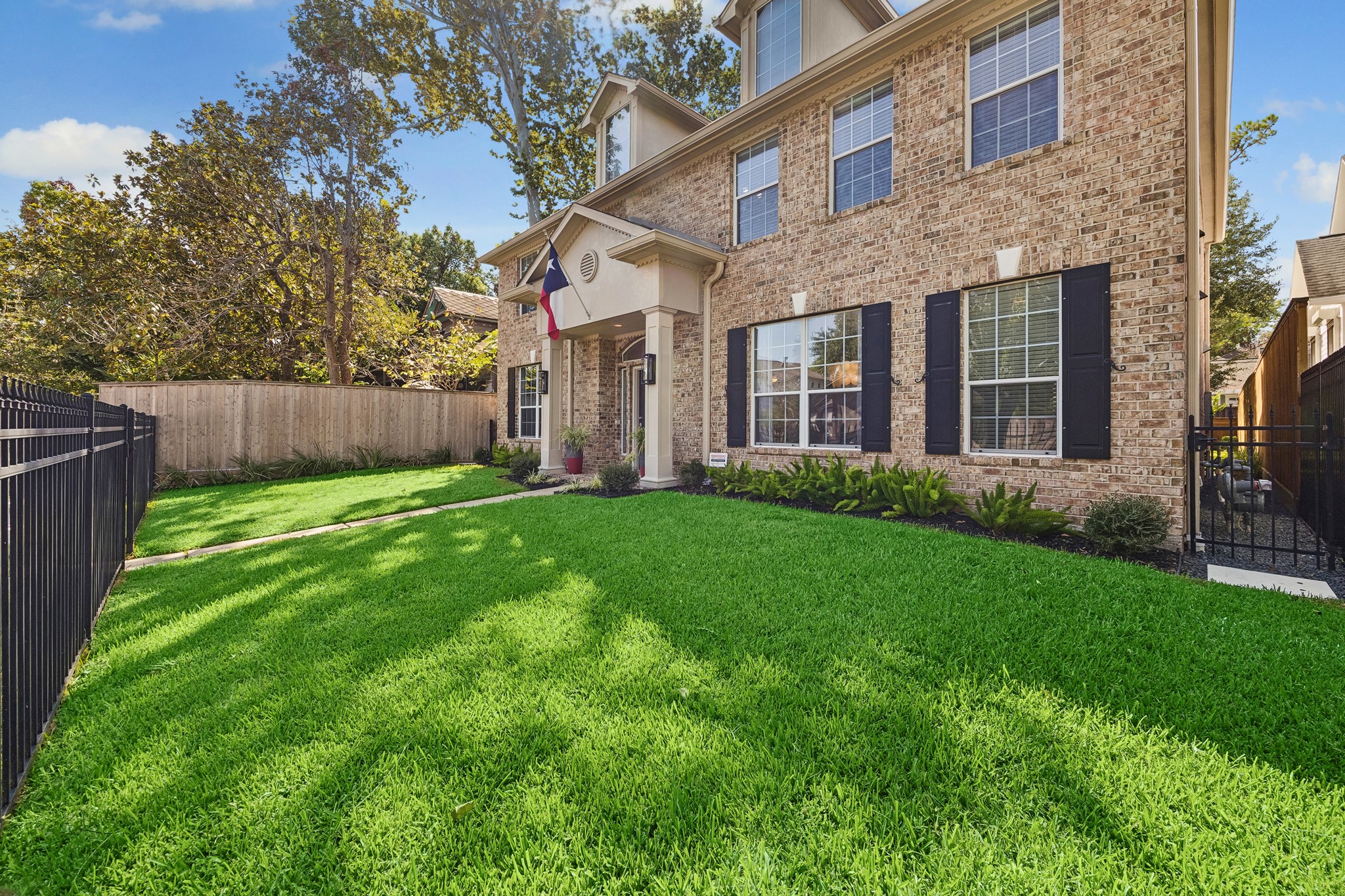 Fully fenced front yard with a lush lawn, mature trees, and established landscaping, creating a welcoming approach to the home.