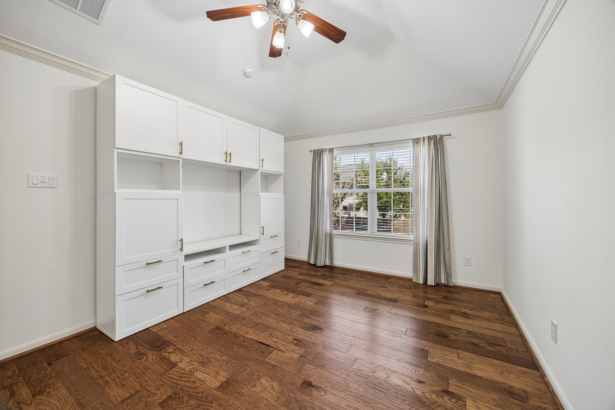 Secondary bedroom with hardwood floors, custom built-in shelving and cabinetry, and a ceiling fan, offering excellent storage and flexibility.