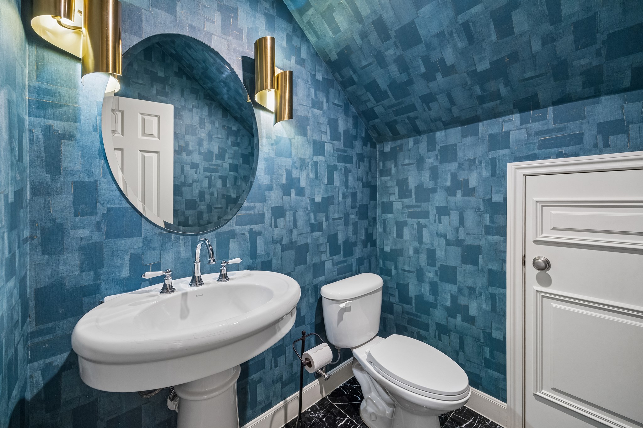 Stylish powder room featuring bold blue textured wallpaper, a statement round mirror, and modern brass lighting.