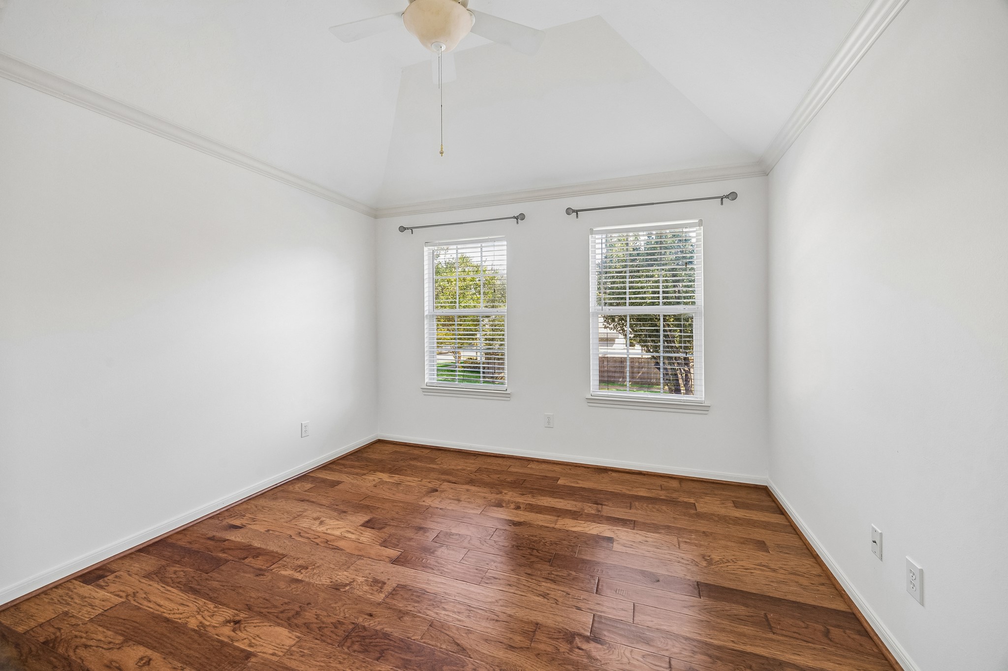 Bright secondary bedroom with hardwood floors, a ceiling fan, and two windows overlooking the yard. Space for a freestanding wardrobe offers a flexible closet solution.