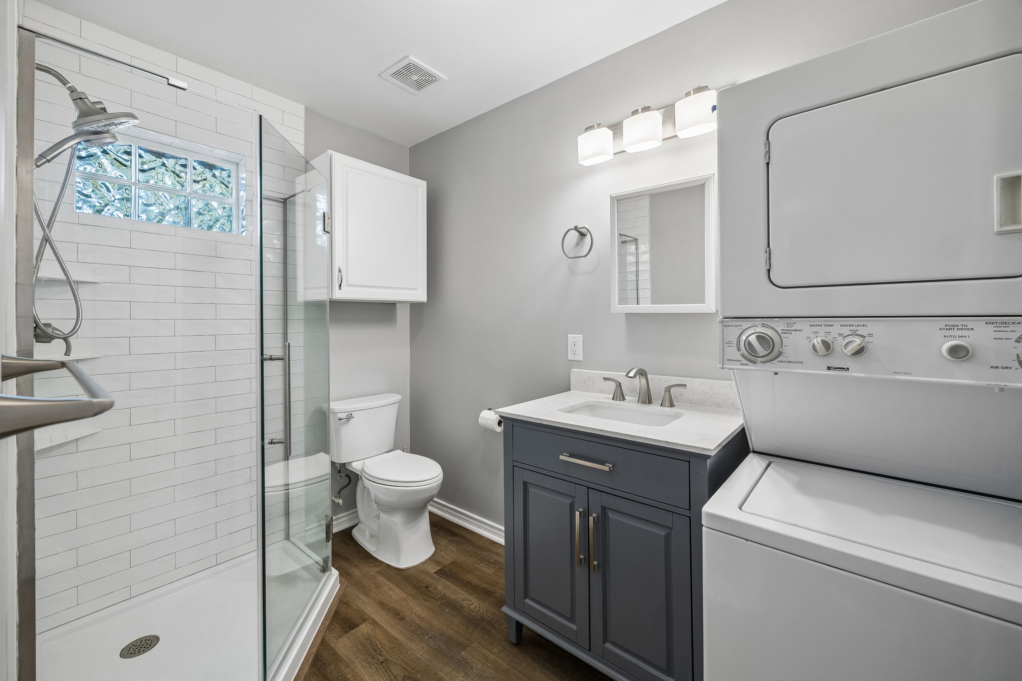 Garage apartment bath with a modern vanity, walk-in shower, and included washer and dryer for added convenience.