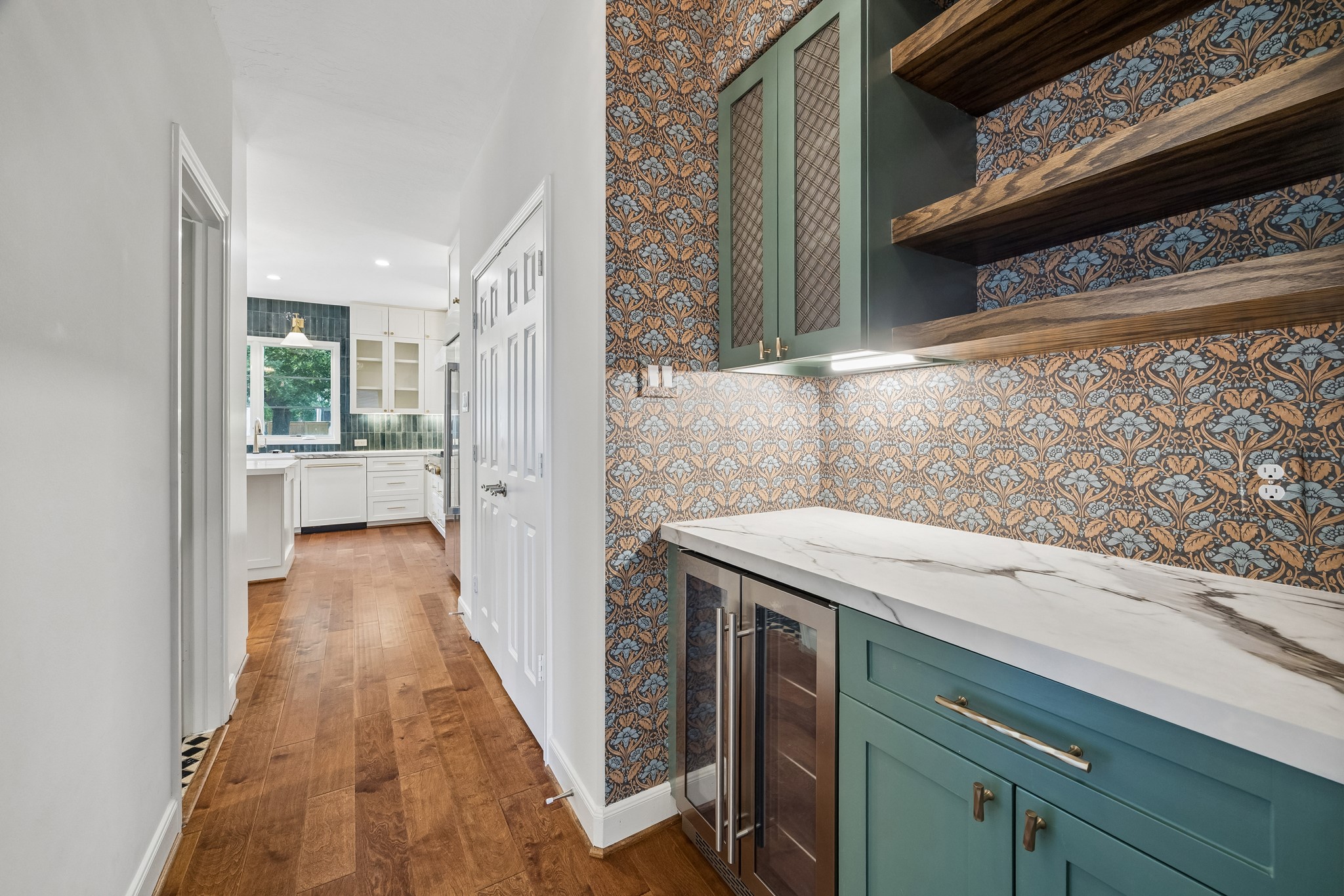 Custom dry bar between the kitchen and dining room, featuring a beverage refrigerator, open shelving, and a stylish backsplash. A spacious pantry provides additional storage nearby.