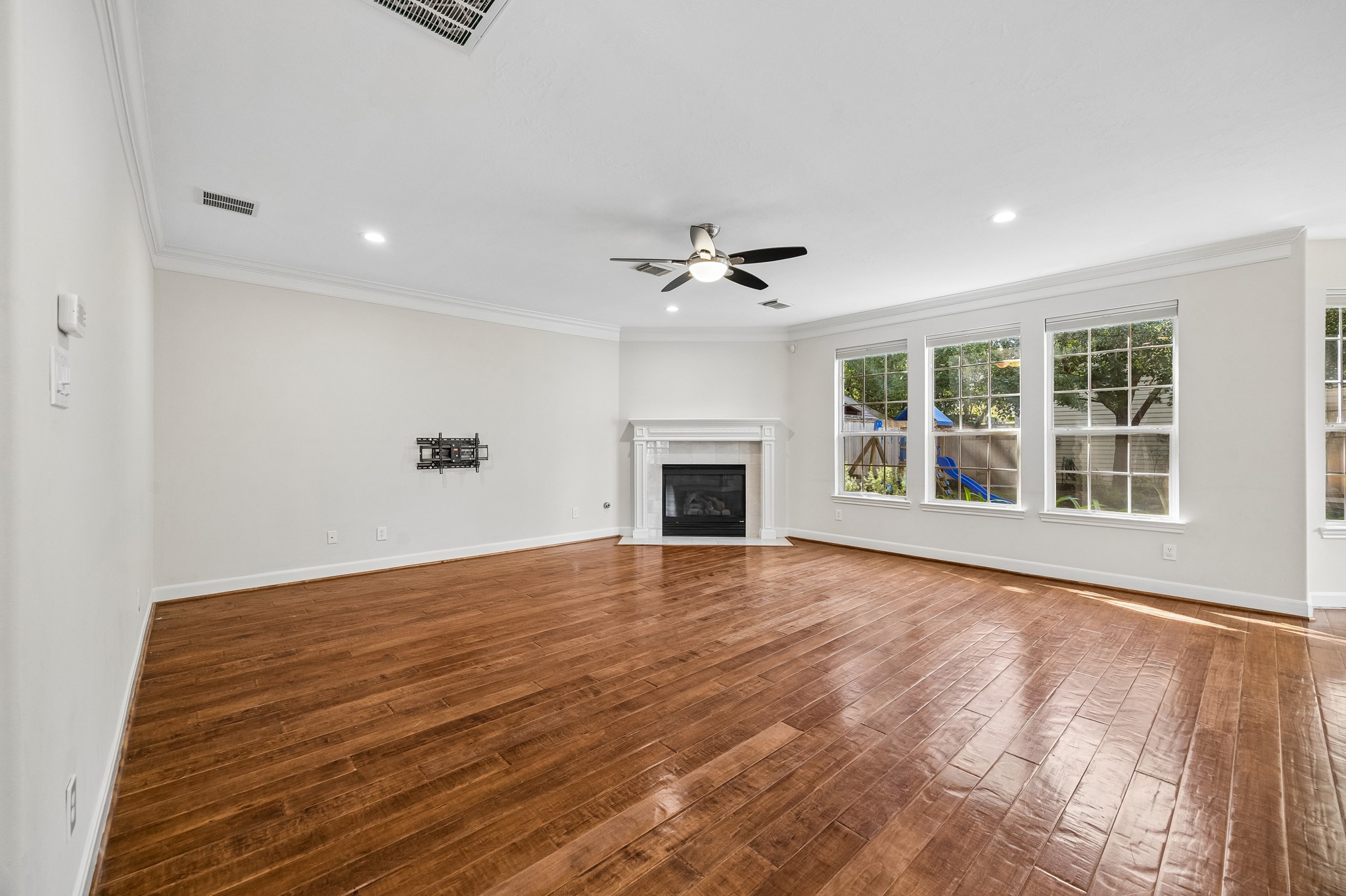 Spacious living area with rich wood floors, a gas-log fireplace, and abundant natural light from large windows overlooking the backyard. Spacious living area with rich wood floors, a gas-log fireplace, and abundant natural light from large windows overlooking the backyard.