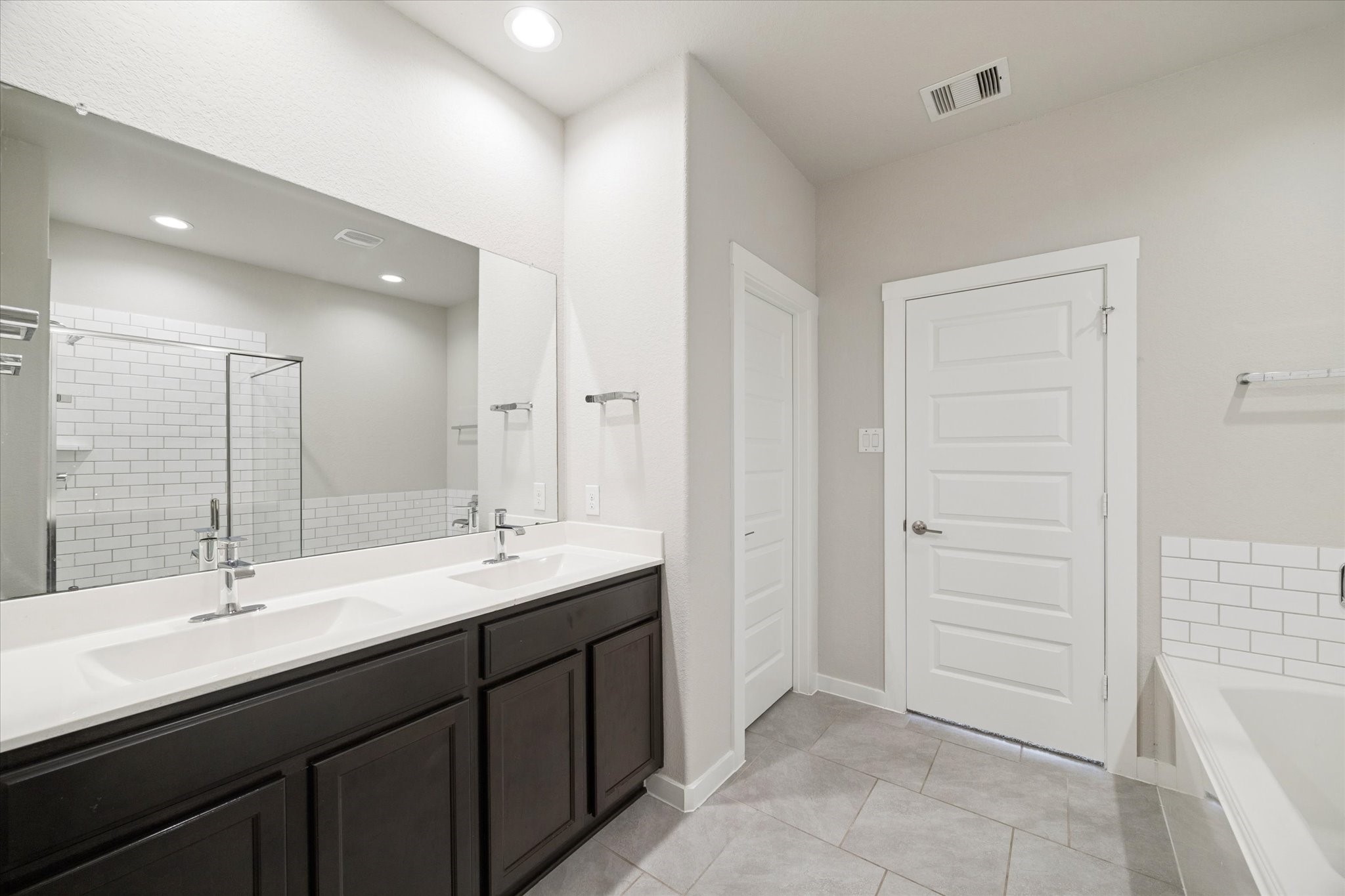 A well appointed primary bath featuring dual sinks with ample counter space and storage. Clean tile flooring, simple lines, and bright lighting create a functional environment designed for easy daily use.