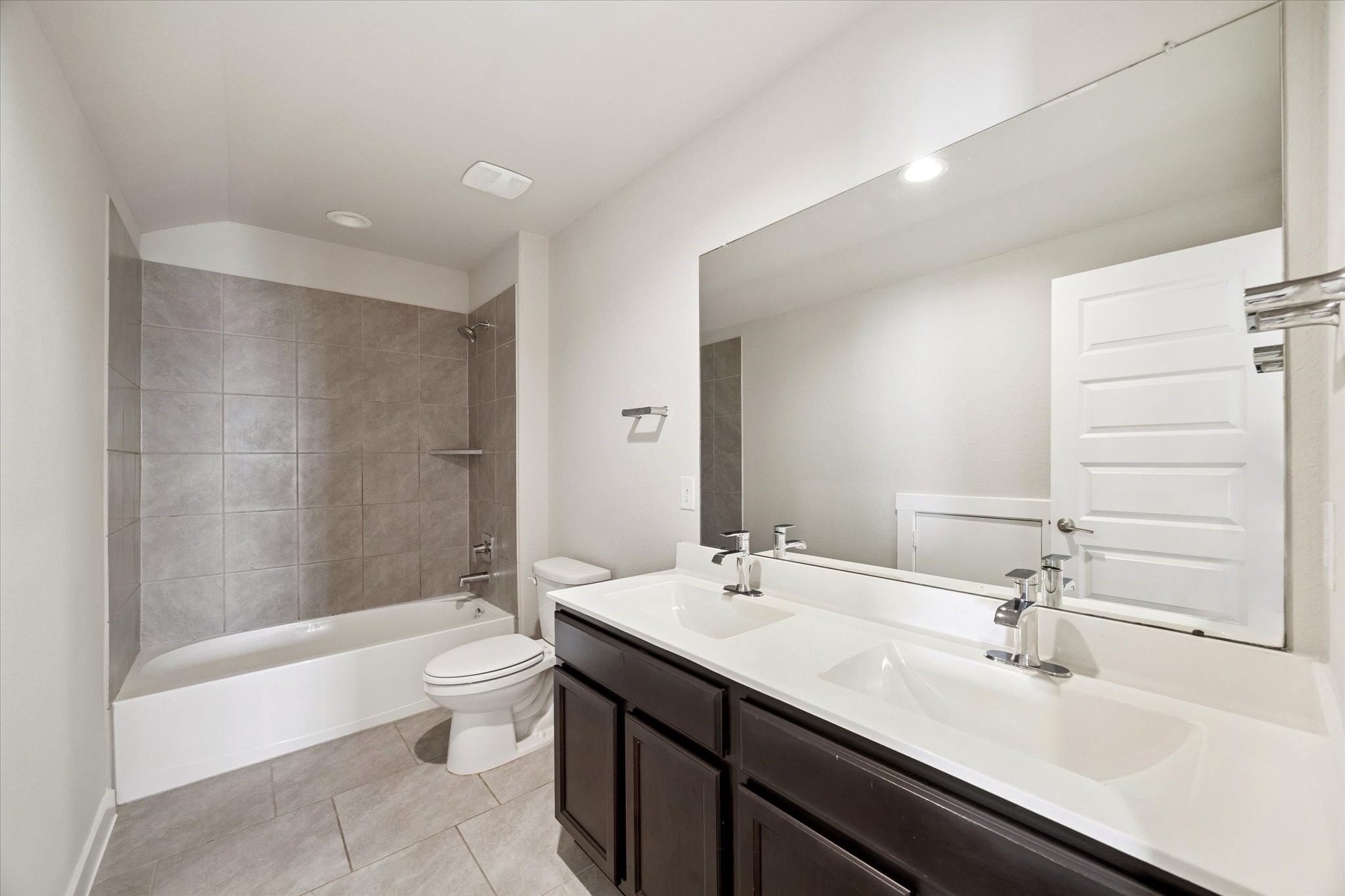 This full bathroom blends practicality with a clean, modern aesthetic. A wide vanity with ample counter space, large mirror, and neutral tile surround the tub-shower combination, creating a bright, functional space well suited for guests or secondary bedrooms.