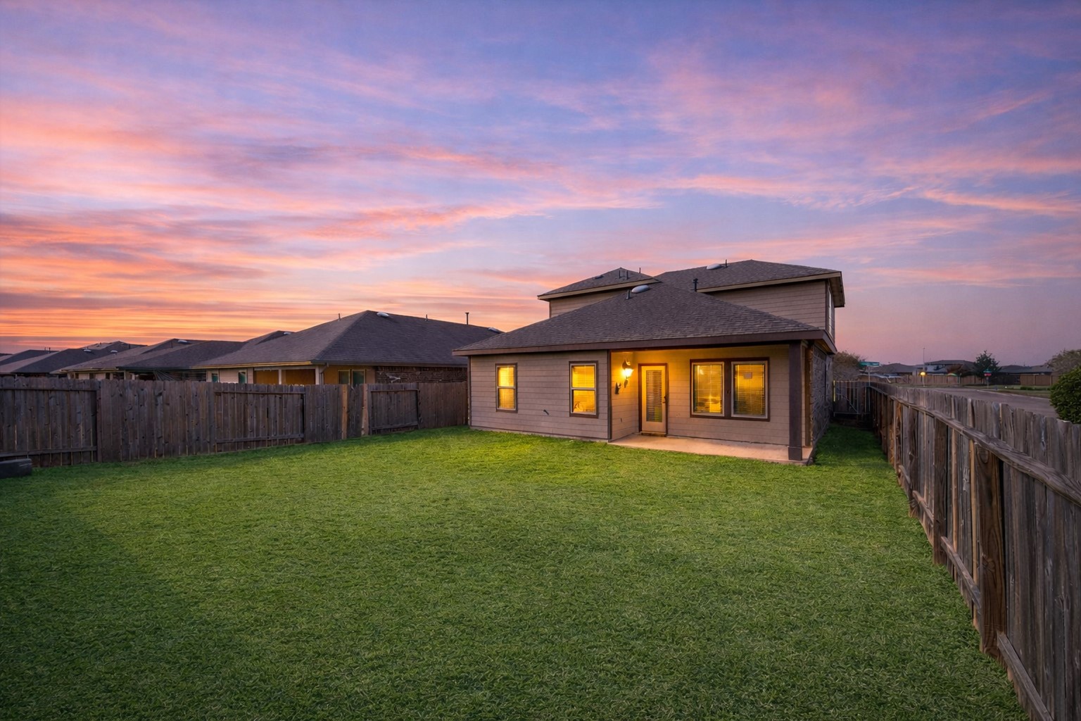 Wide, fully fenced backyard with plenty of green space to stretch out, play, or add a future pool. Covered patio glows at dusk, creating a relaxed setting for evening dinners or weekend gatherings.