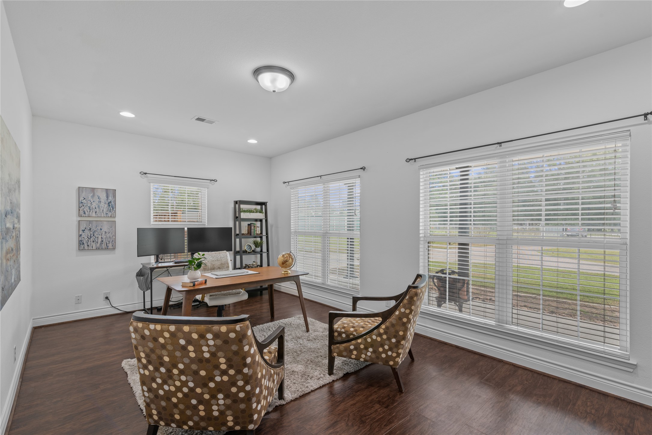 Bright and spacious home office with large windows overlooking the front porch and lawn, offering ample room for a desk and additional seating.