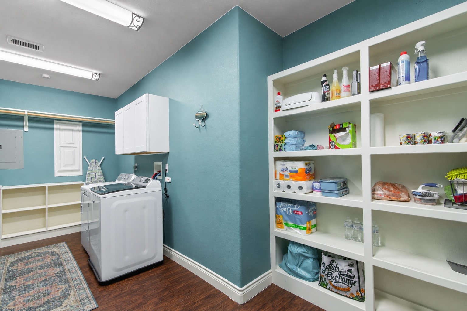 Large laundry room featuring extensive built-in shelving, overhead cabinetry, and a hanging rod for convenient clothing care and household storage.