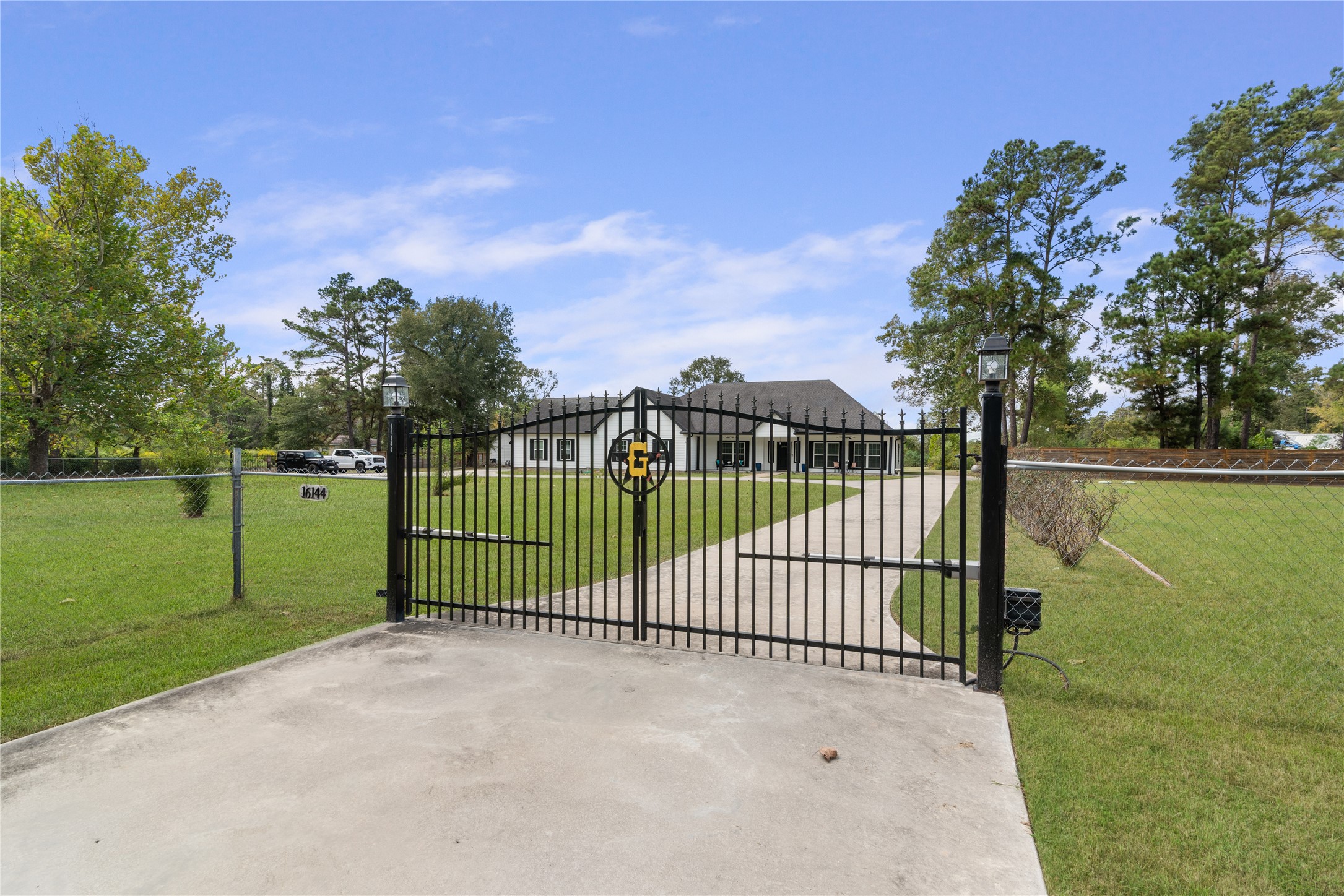 Decorative automatic entry gate with lantern-topped posts creates a welcoming entrance, with a long concrete driveway leading to the home.