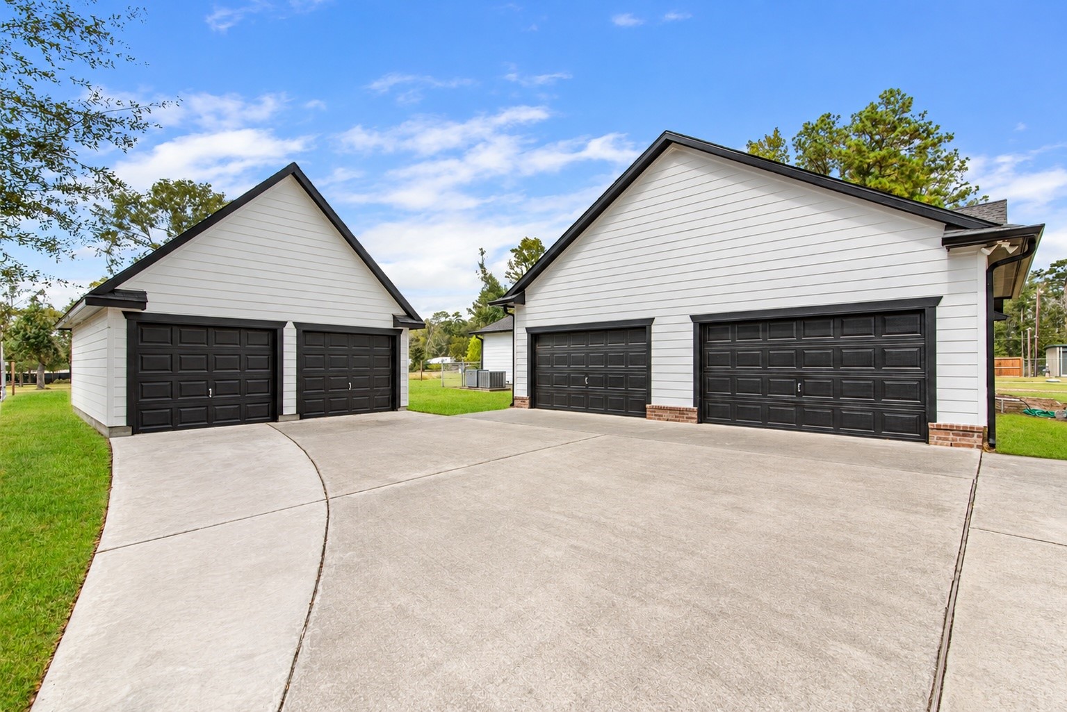 An oversized attached two-car garage and a detached two-car garage provide four total garage spaces, with an expansive concrete driveway for additional parking and easy maneuvering.