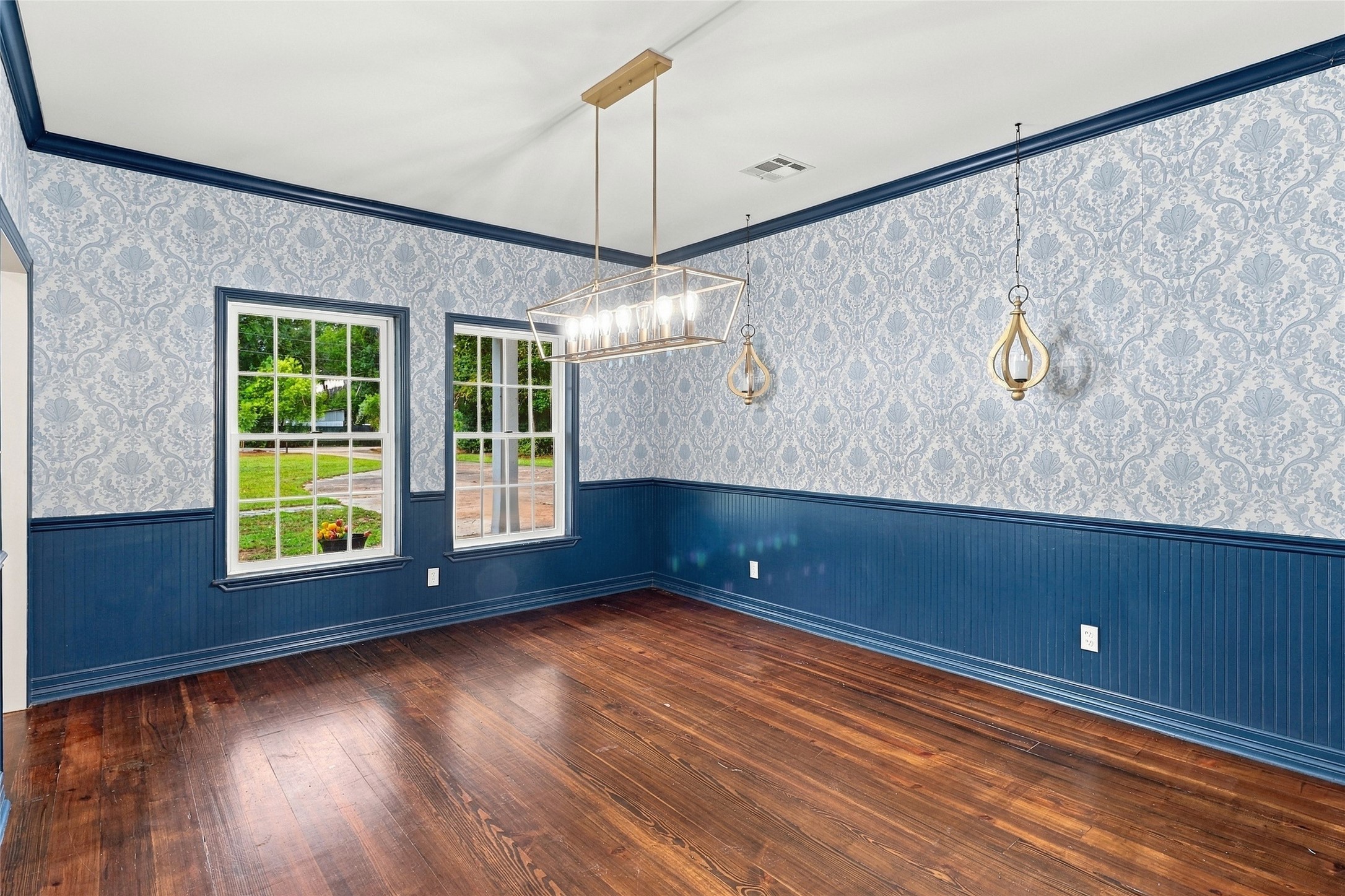 This elegant dining room features beautiful wainscoting and tasteful wallpaper, illuminated by abundant natural light.