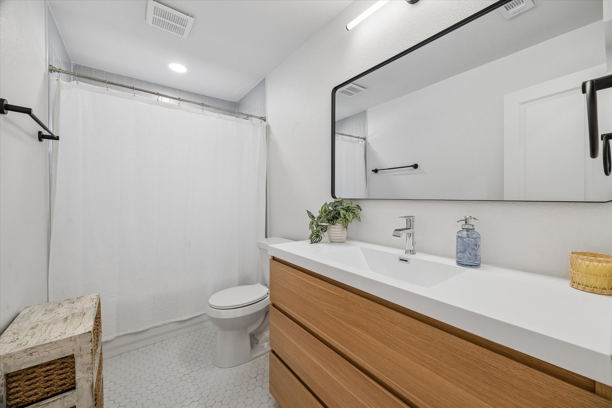 Clean lines give the hall bath a fresh, modern feel, pairing a warm wood vanity with a sleek integrated sink, oversized mirror and classic penny tile flooring.