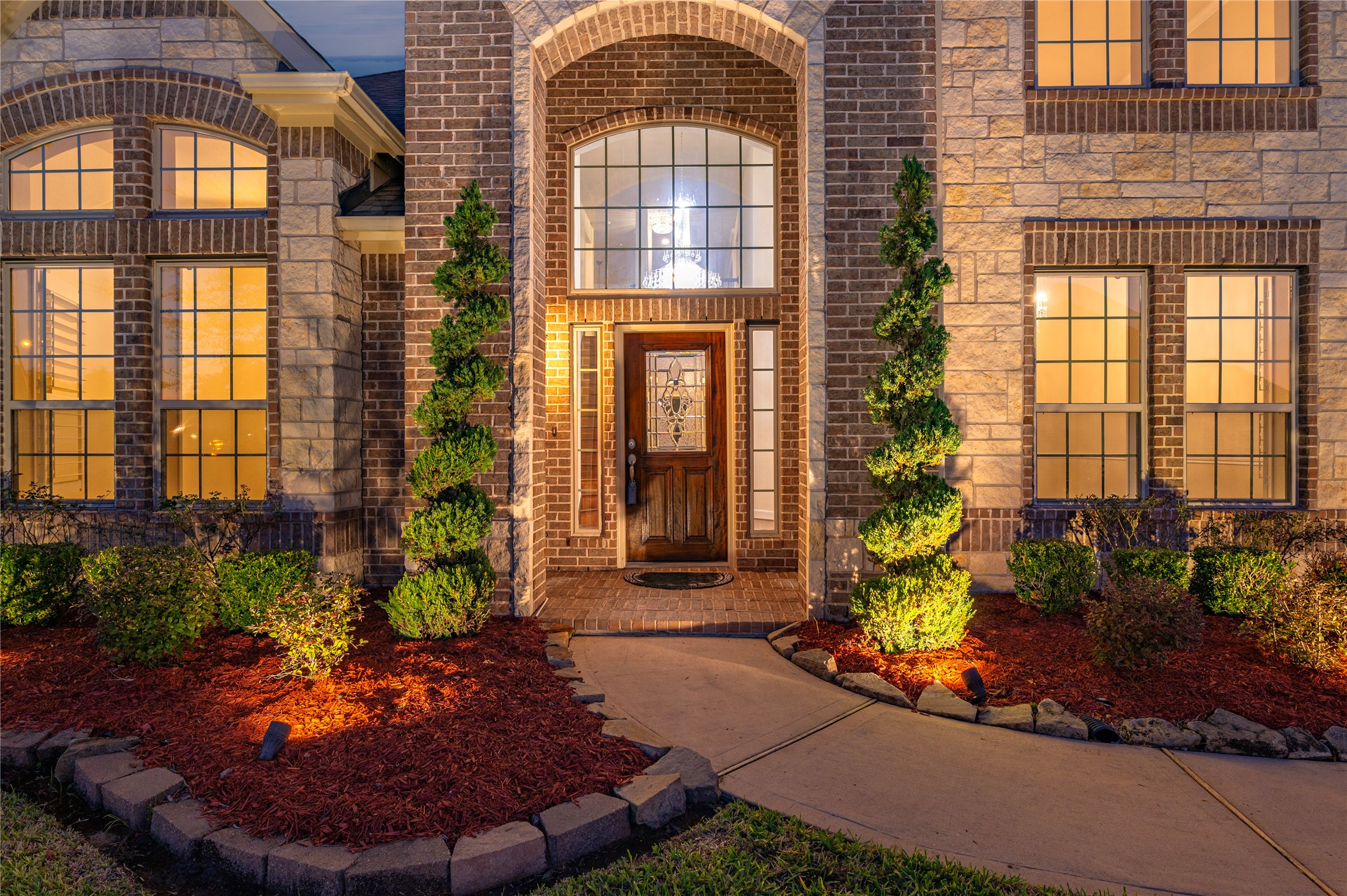 Detailed view of elevation B with professionally maintained lawn, extensive landscaping lighting, exterior stone accent and 2-story covered front porch.