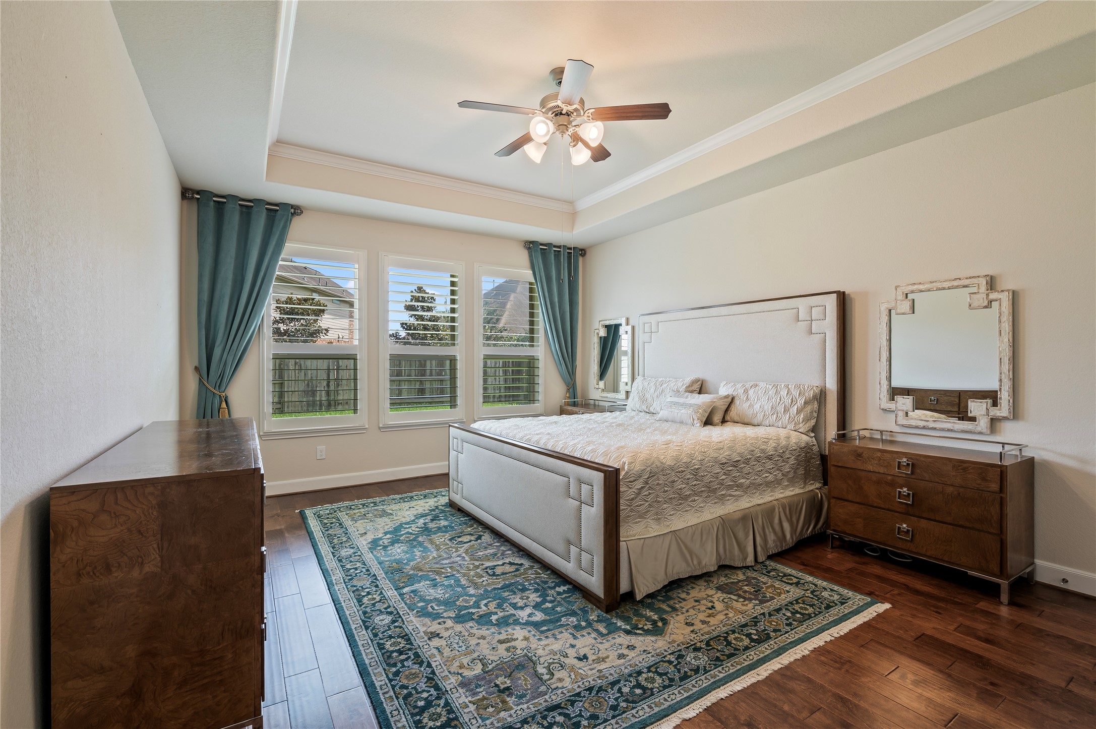 Luxurious primary suite showcasing rich hardwood floors, crown molding and plantation shutters.