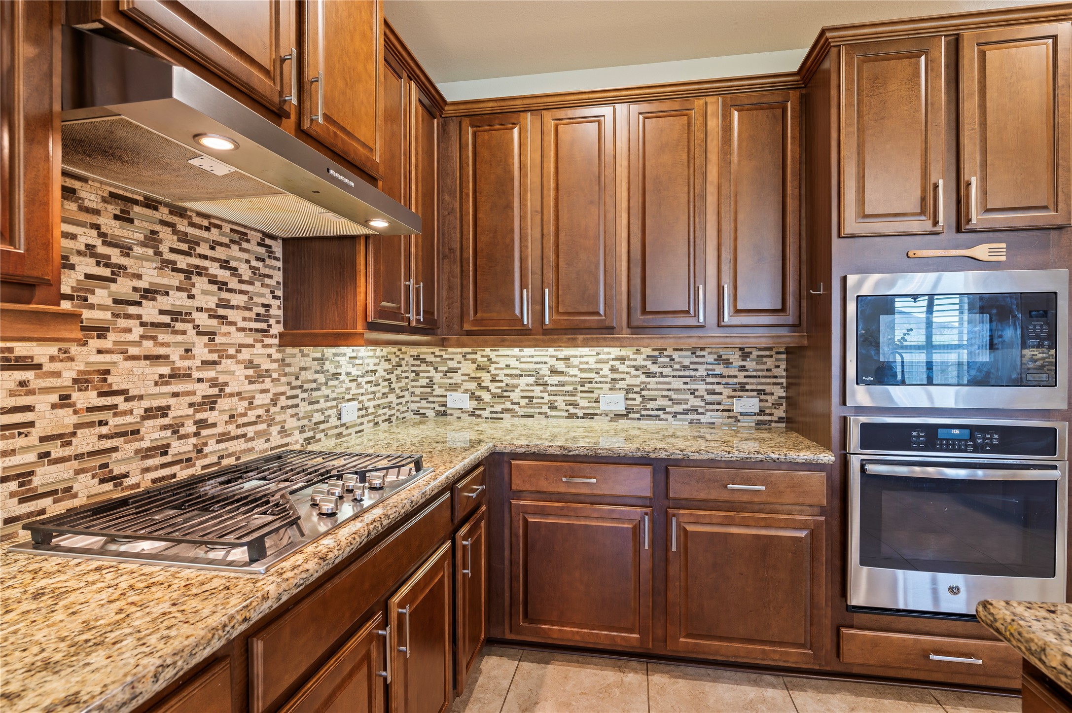 Attractive backsplash compliments the 5-burner gas range; built-in oven and microwave surrounded by maple kitchen cabinetry.