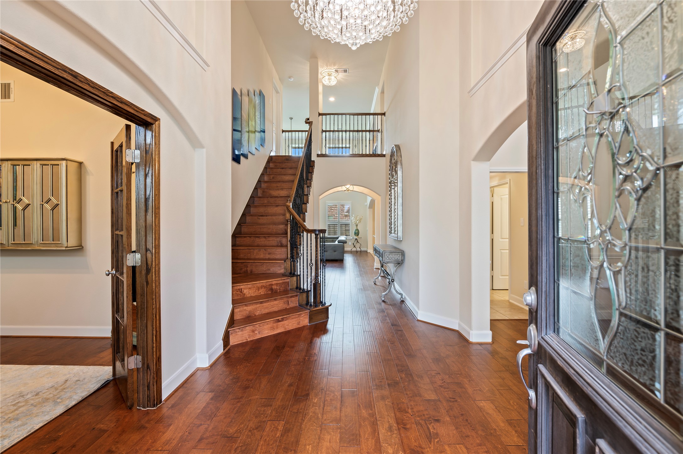 Inviting entrance features soaring ceilings, custom chandelier and hardwood floors including the staircase with wrought iron railing and catwalk.