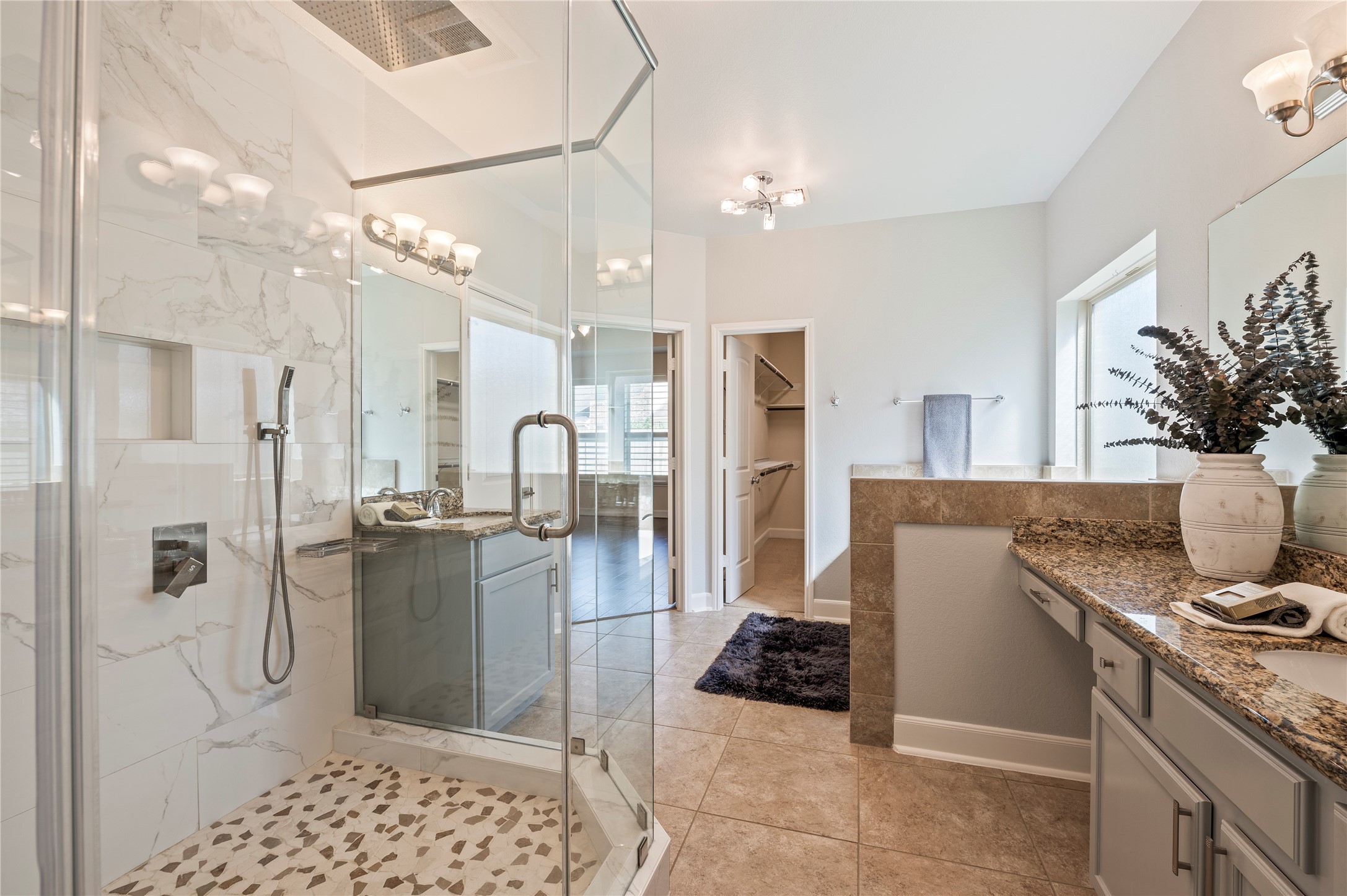 Spectacularly updated 6'x4' seamless glass shower featuring dual rainfall shower heads and removable handheld wands with river rock accented flooring.