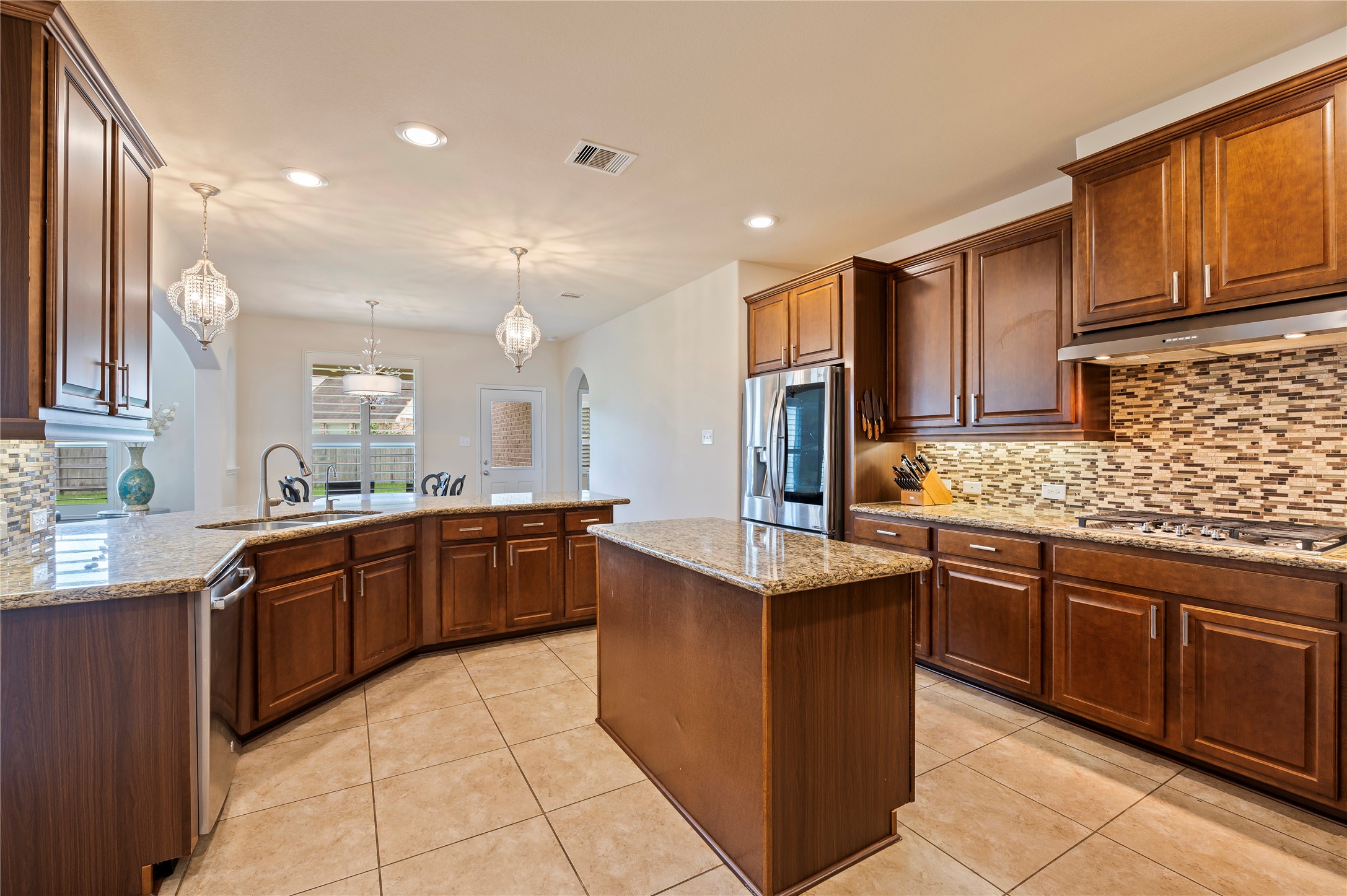 Spacious island kitchen with custom pendent lighting over the breakfast bar, hardware on the cabinets and stainless steel appliances.