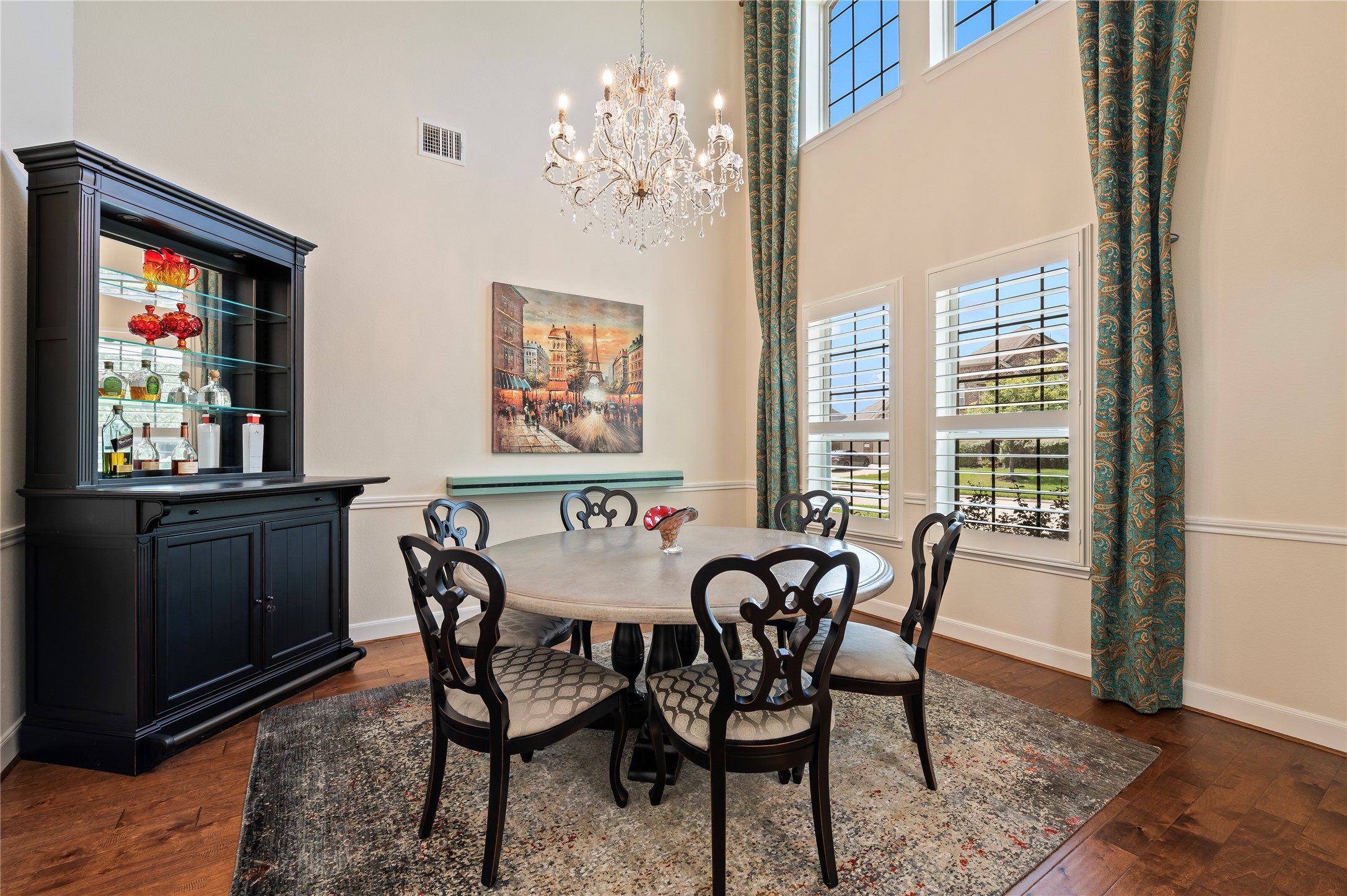 Elegant two-story formal dining room features custom chandelier, hardwood flooring, chair-rail molding and plantation shutters.