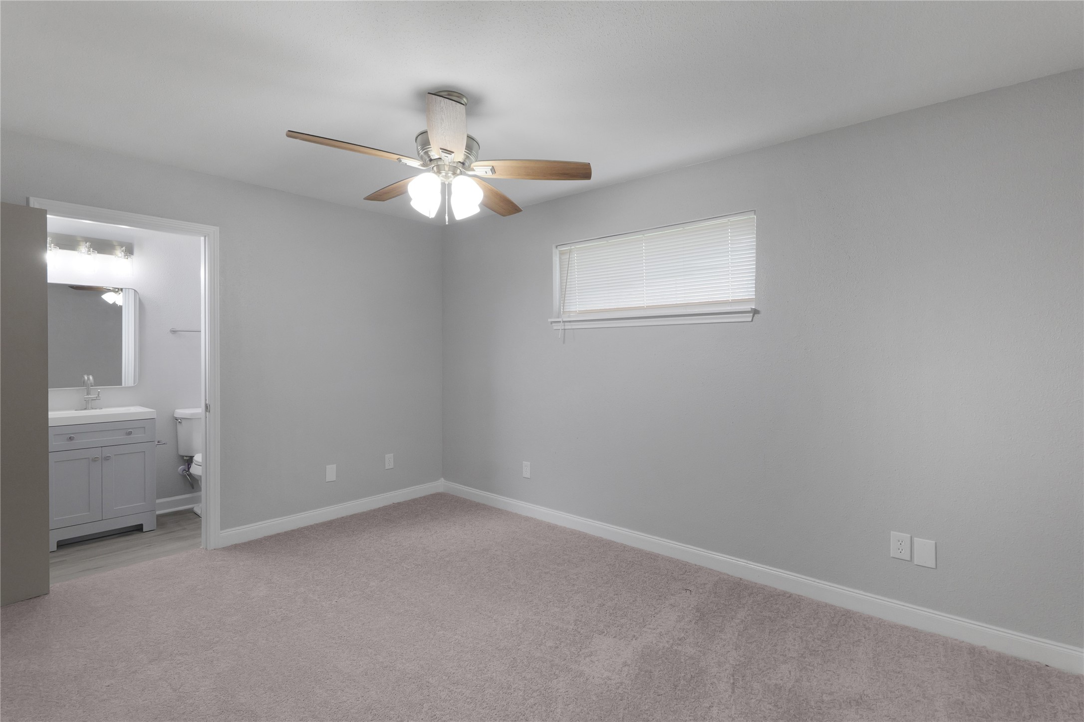 The primary bedroom offers a ceiling fan, neutral colors, and convenient access to its adjoining bathroom.