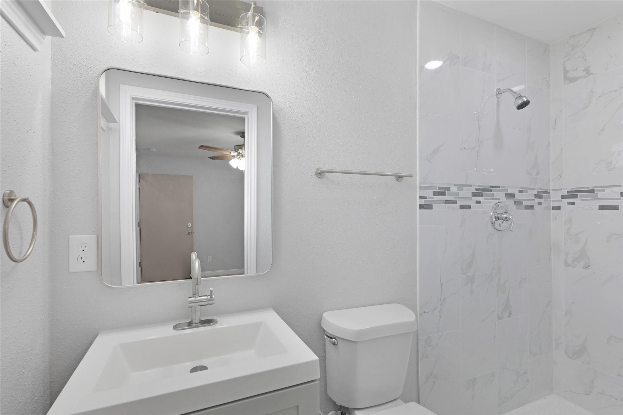 A tiled walk-in shower with a decorative accent pairs with an updated vanity and framed mirror.