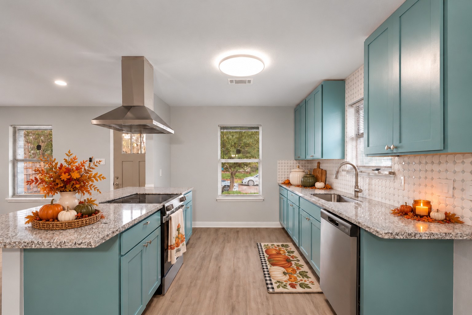 Updated kitchen featuring colorful cabinetry, stainless steel appliances, a tile backsplash, and an island with a range and vent hood. Digitally staged.