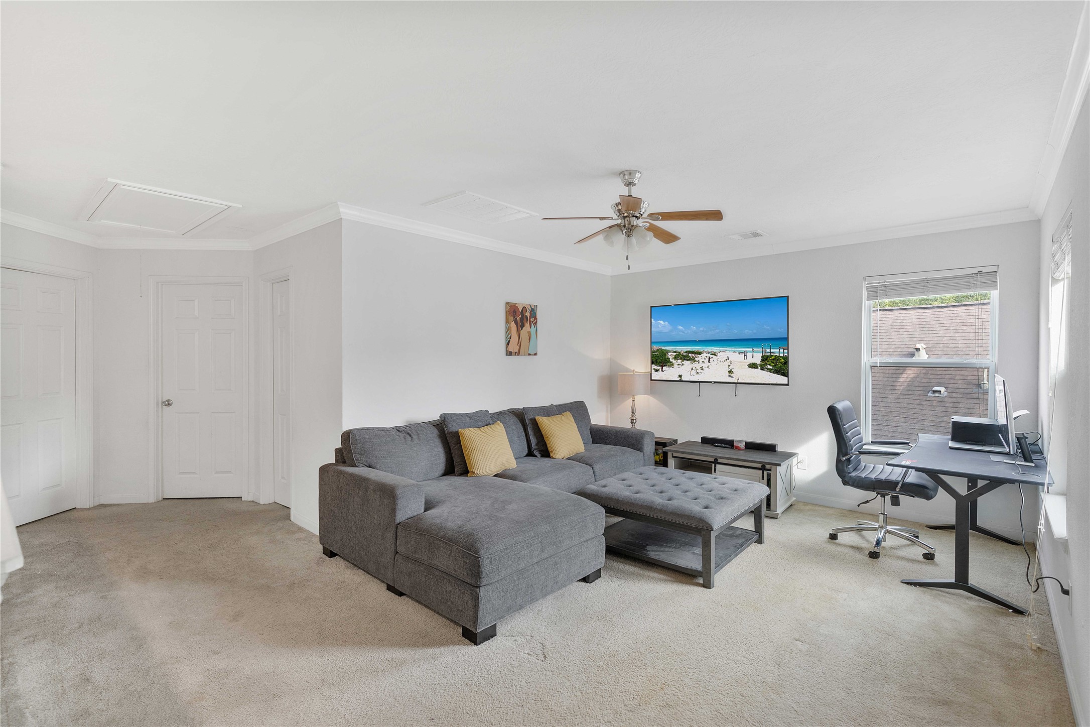 Spacious living area with a comfortable sectional sofa and entertainment setup, featuring a work-from-home desk by a bright window.