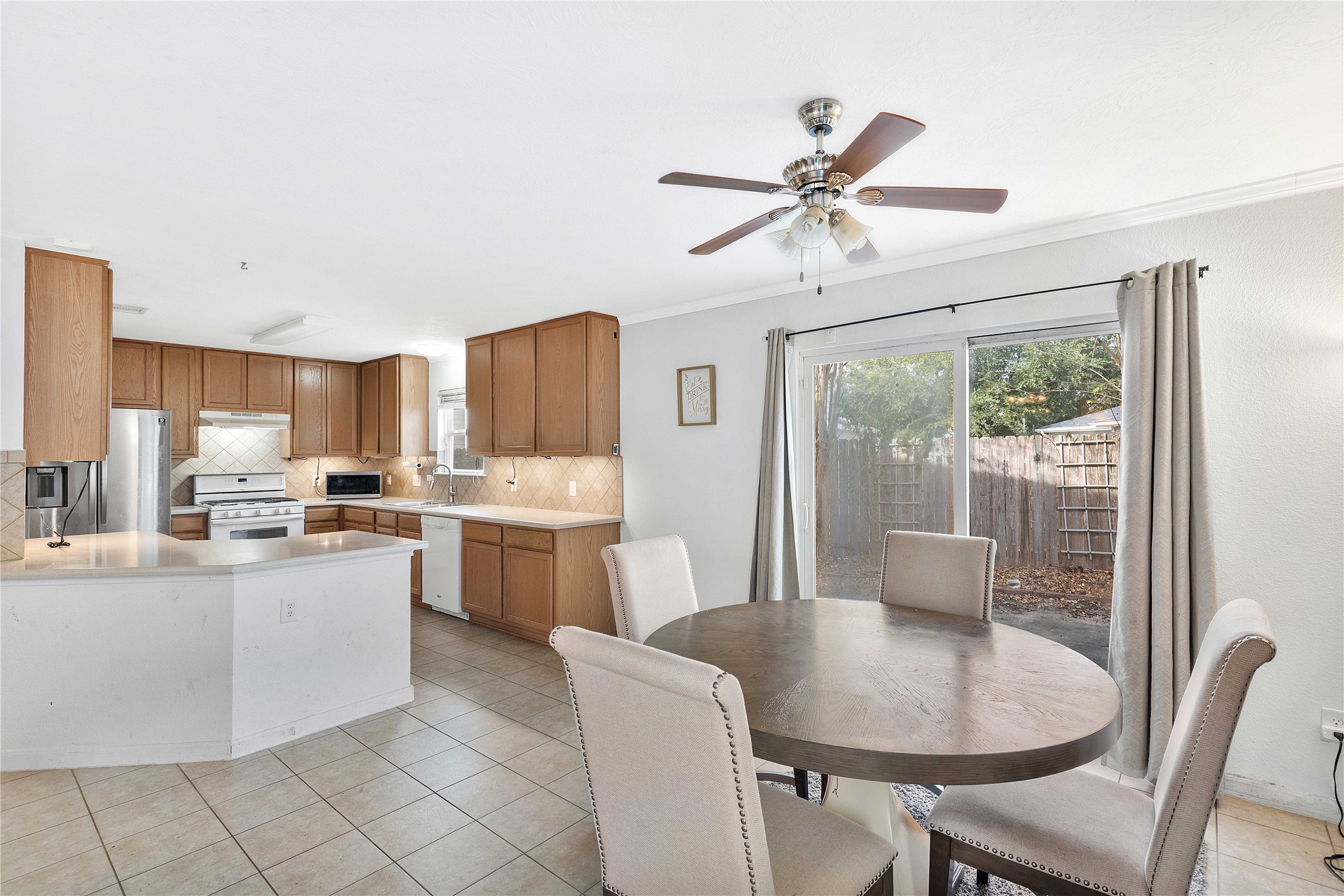 Bright and inviting kitchen and dining area featuring elegant wood cabinetry, modern stainless steel appliances, and a cozy dining space with a view of the backyard through sliding glass doors.