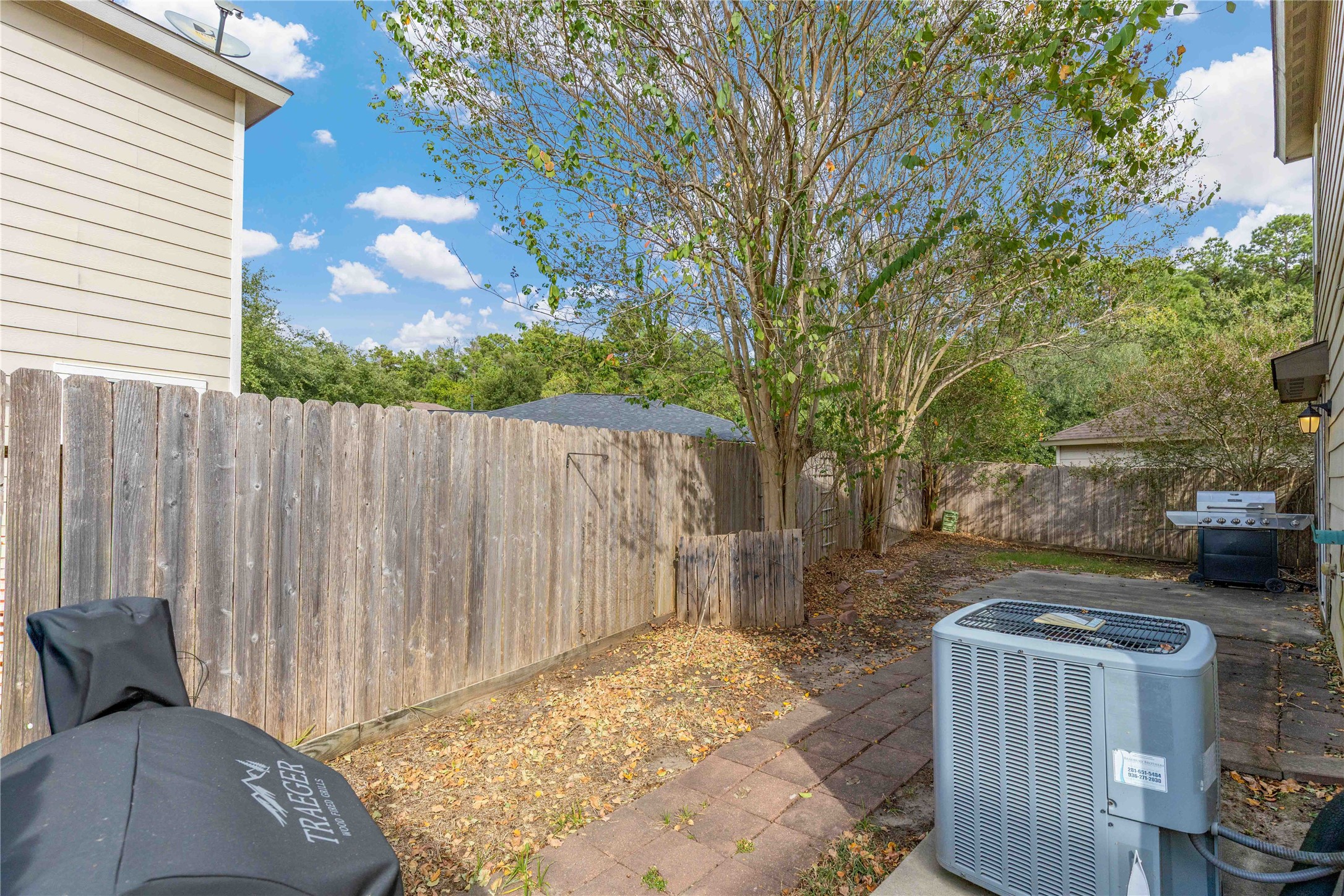 Charming backyard space featuring mature trees, a privacy fence, and a patio area perfect for outdoor grilling and relaxation.