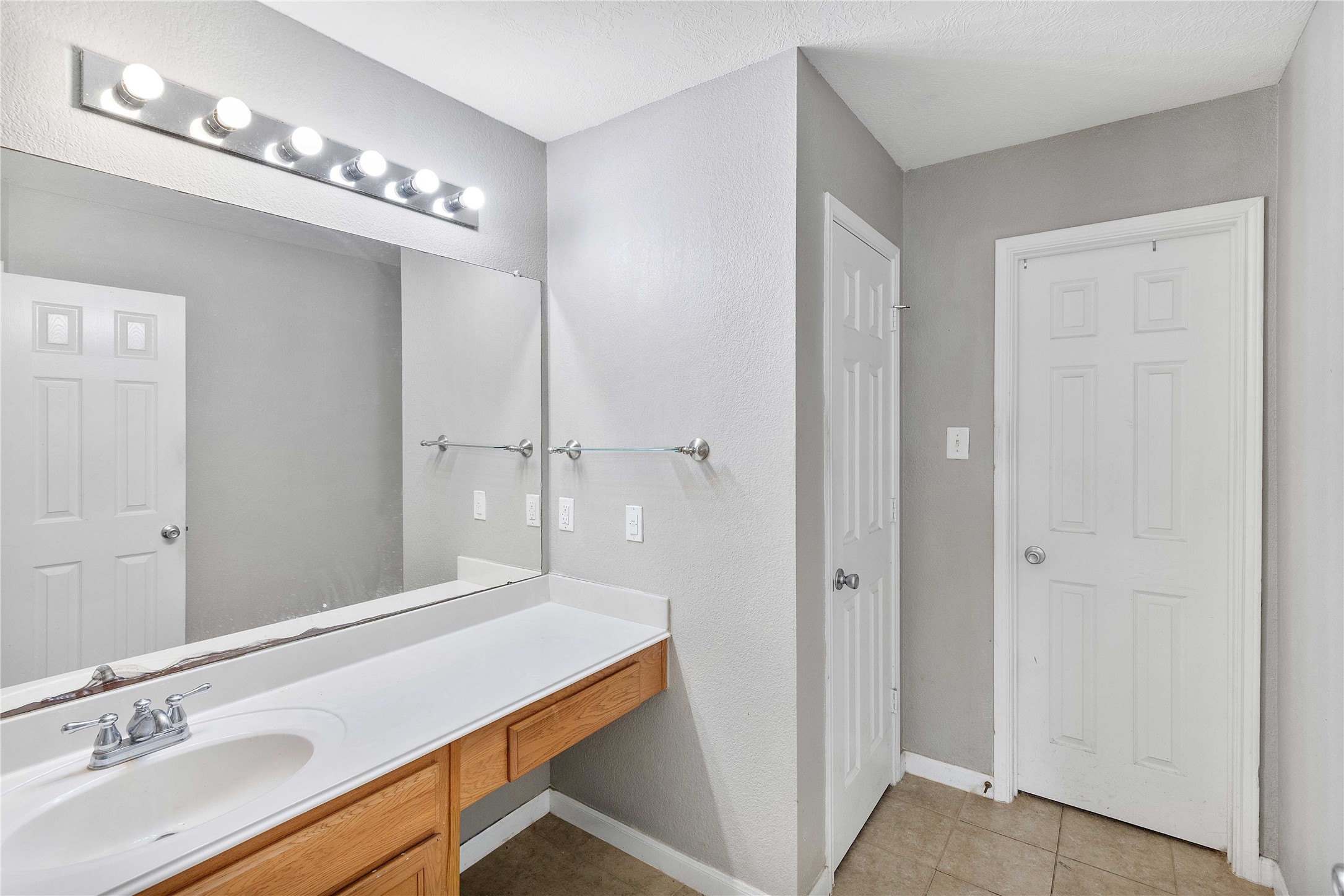 Modern bathroom featuring a spacious vanity with ample counter space, sleek lighting, and neutral tile flooring.