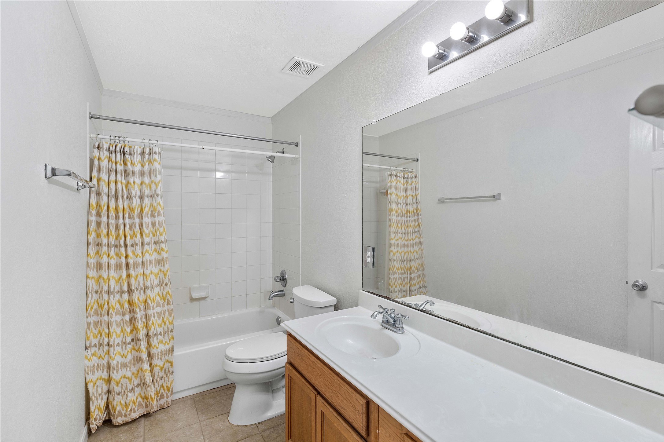 Bright bathroom featuring a spacious vanity, modern lighting, and a bathtub with a stylish patterned shower curtain.