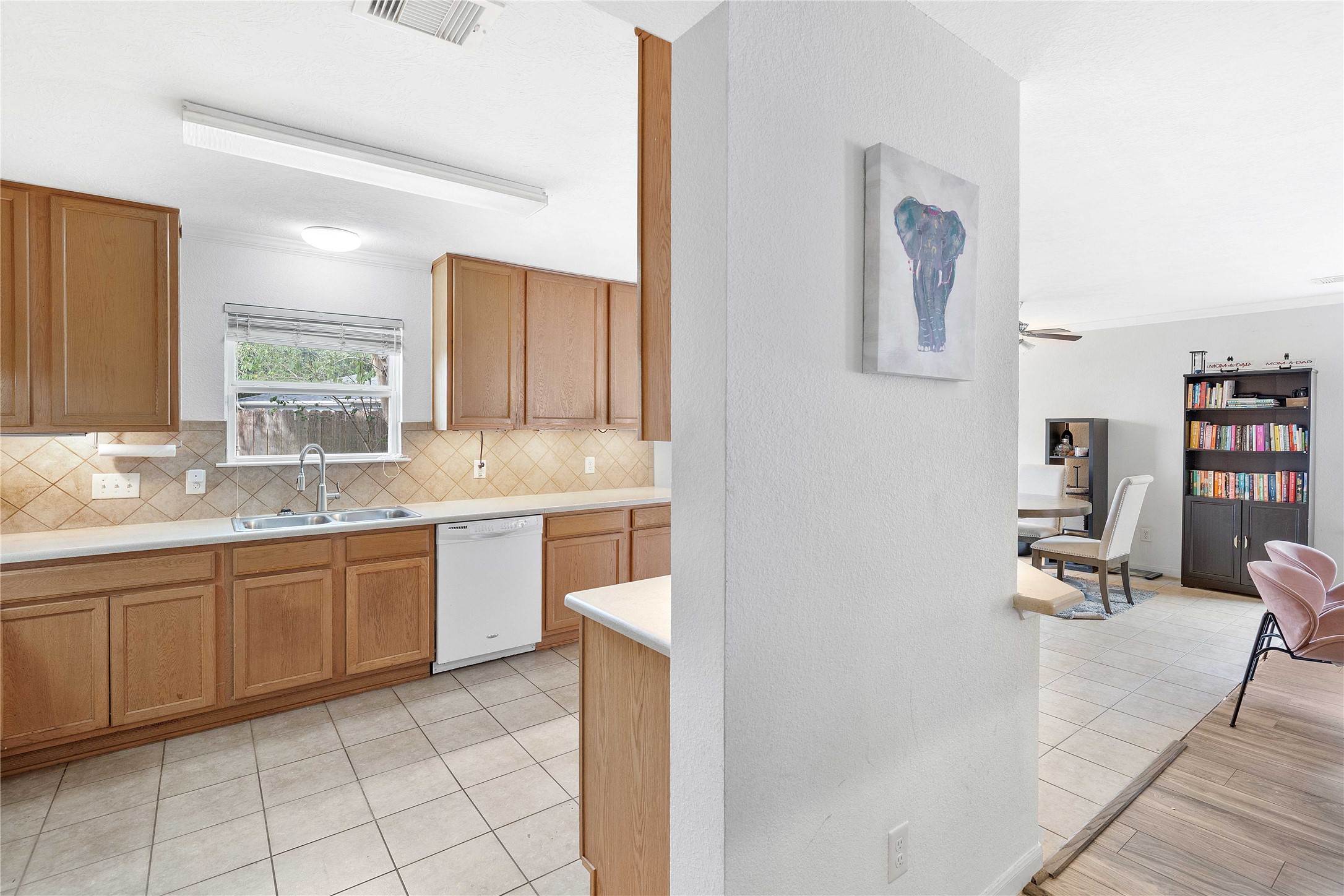 Bright kitchen with warm wood cabinetry and tiled backsplash, seamlessly flowing into a cozy living area featuring built-in shelving and modern seating.