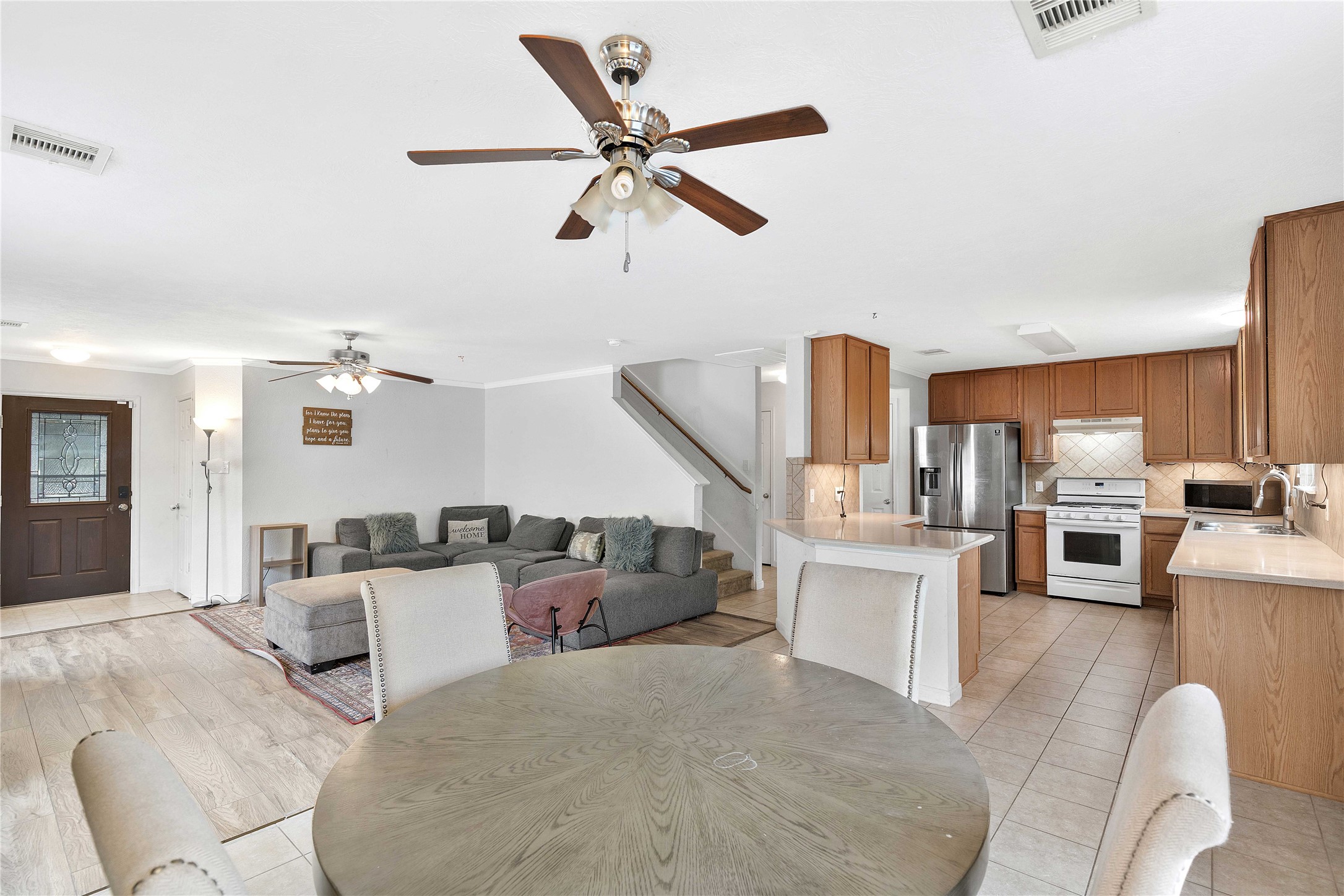 Spacious open-concept living area with modern kitchen featuring stainless steel appliances and ample cabinetry. Cozy living room with plush sectional and ceiling fan for comfort.