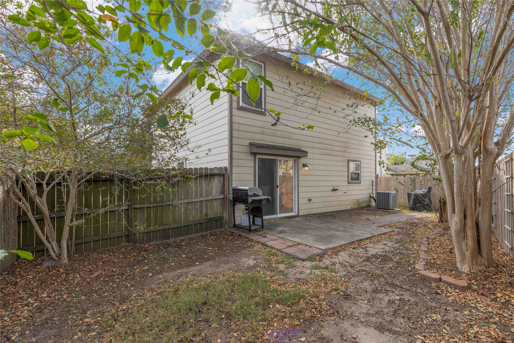 Charming backyard features a cozy patio area perfect for outdoor grilling and entertaining, surrounded by mature trees and a privacy fence for a serene setting.