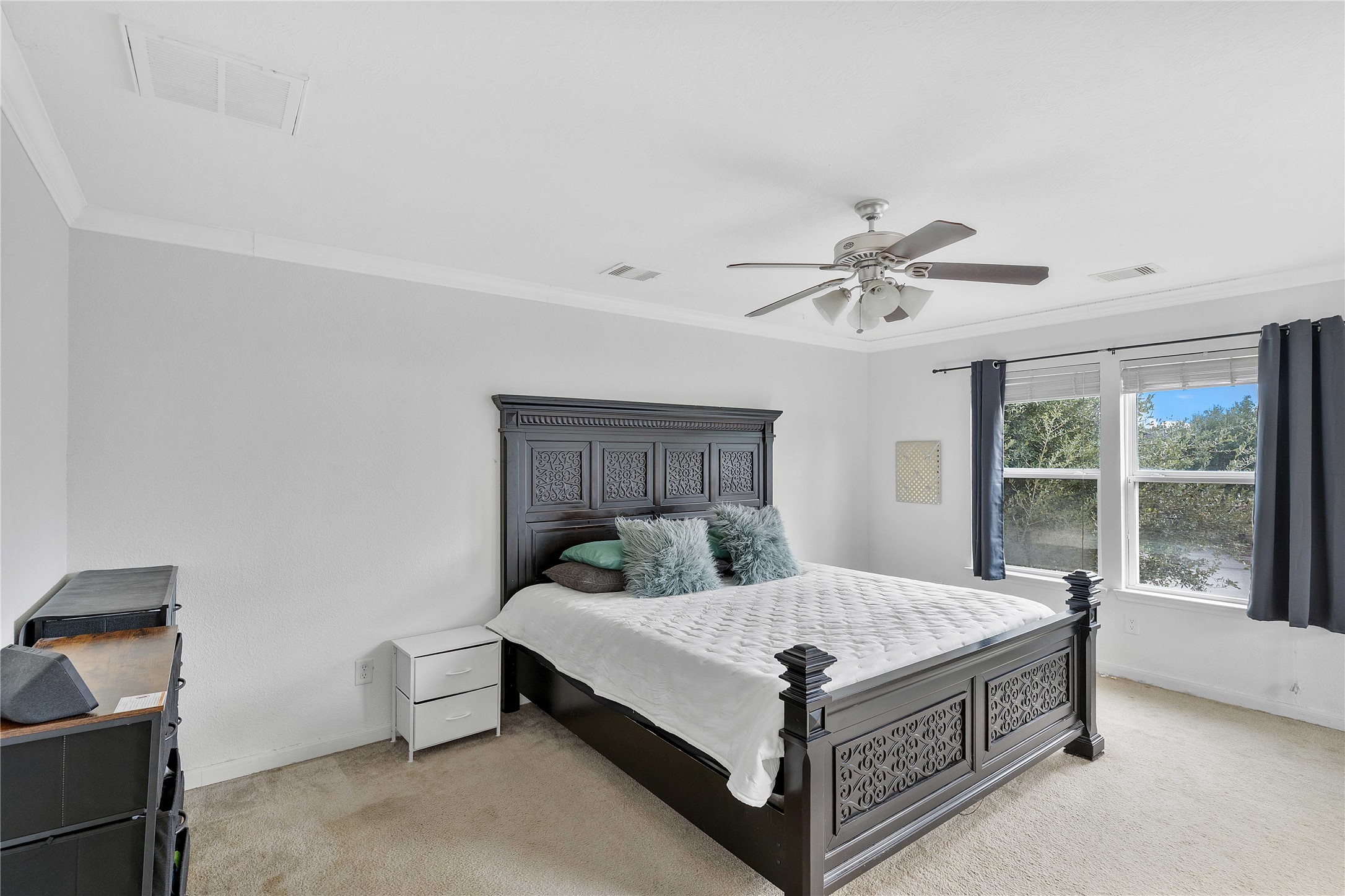 Spacious bedroom featuring a large window for natural light, elegant dark wood furniture, and a ceiling fan for comfort.
