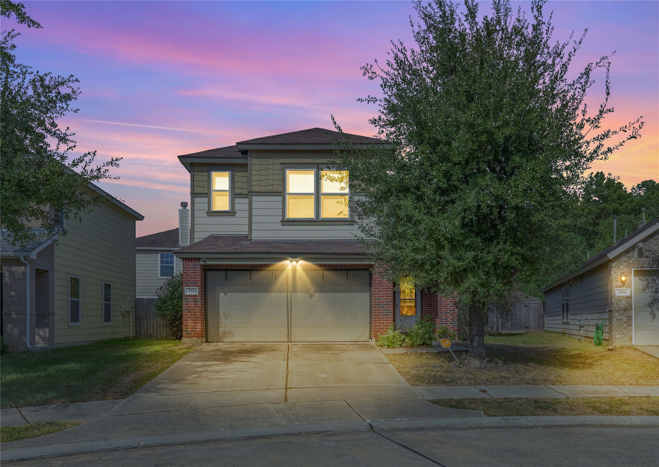 Charming two-story home with a spacious driveway, illuminated at dusk, surrounded by mature trees and featuring a welcoming facade.