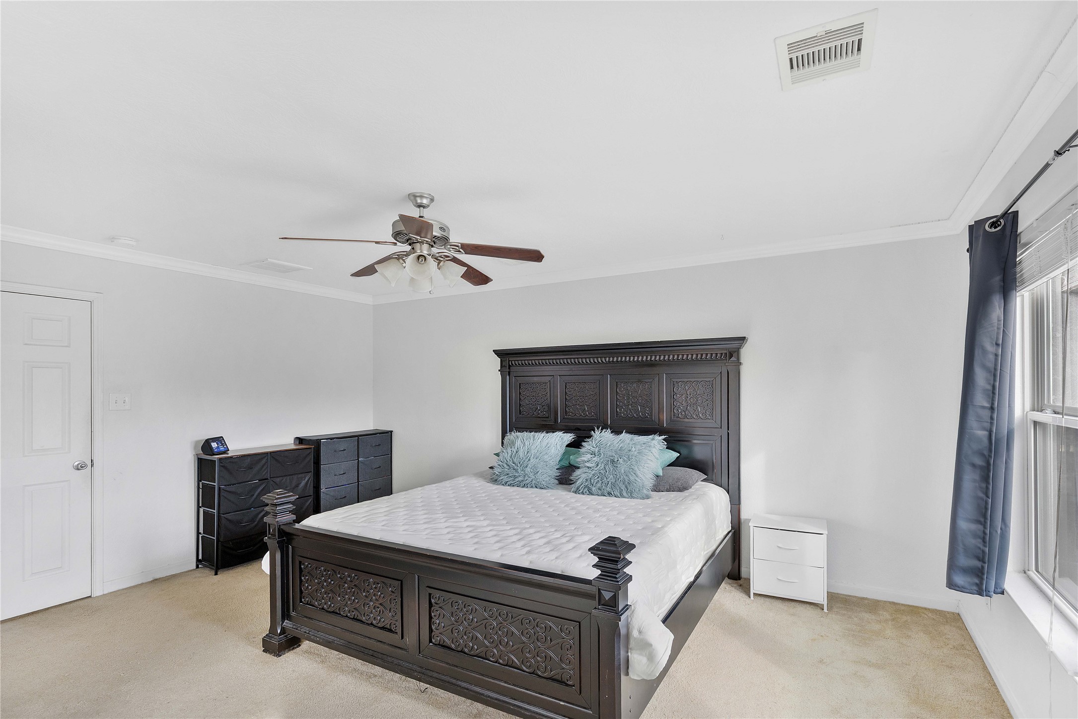 Spacious bedroom featuring a classic dark wood bed frame, carpeted flooring, and ample natural light from large windows.