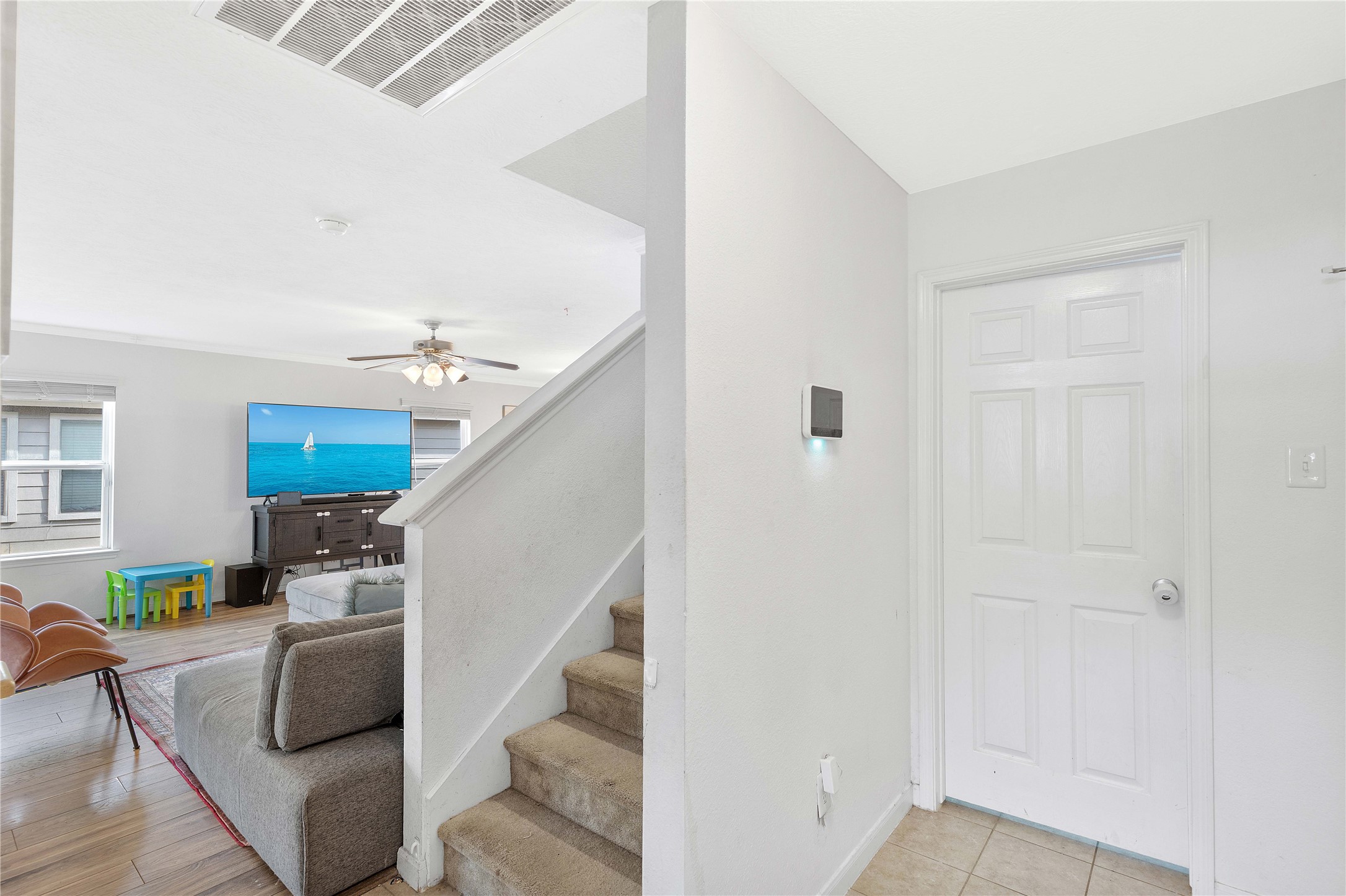 Inviting entryway leads into a cozy living room with abundant natural light, featuring a ceiling fan and stylish wood flooring, perfect for family relaxation.