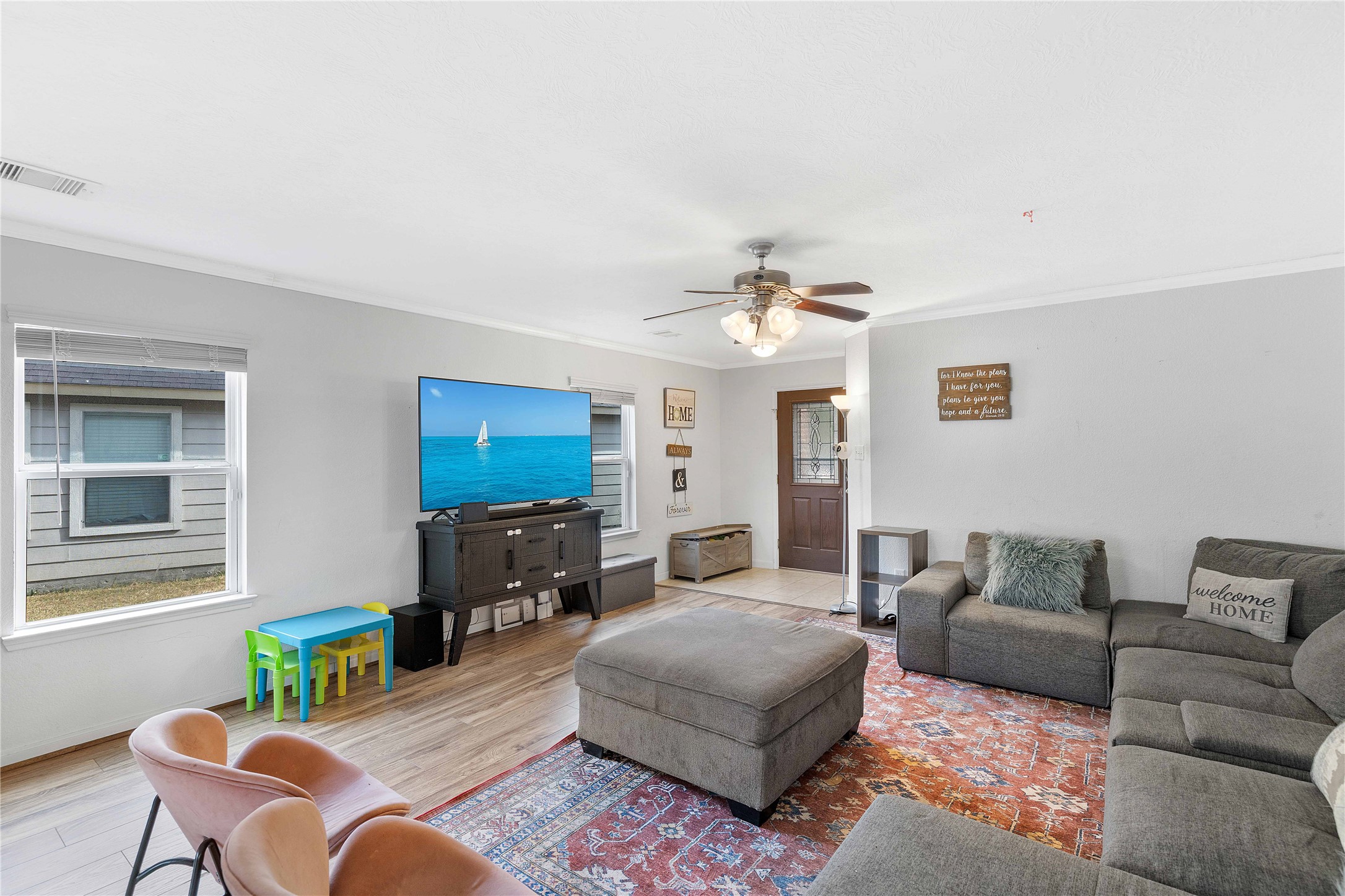 Spacious living room with abundant natural light, featuring a cozy sectional sofa, stylish ceiling fan, and inviting decor.