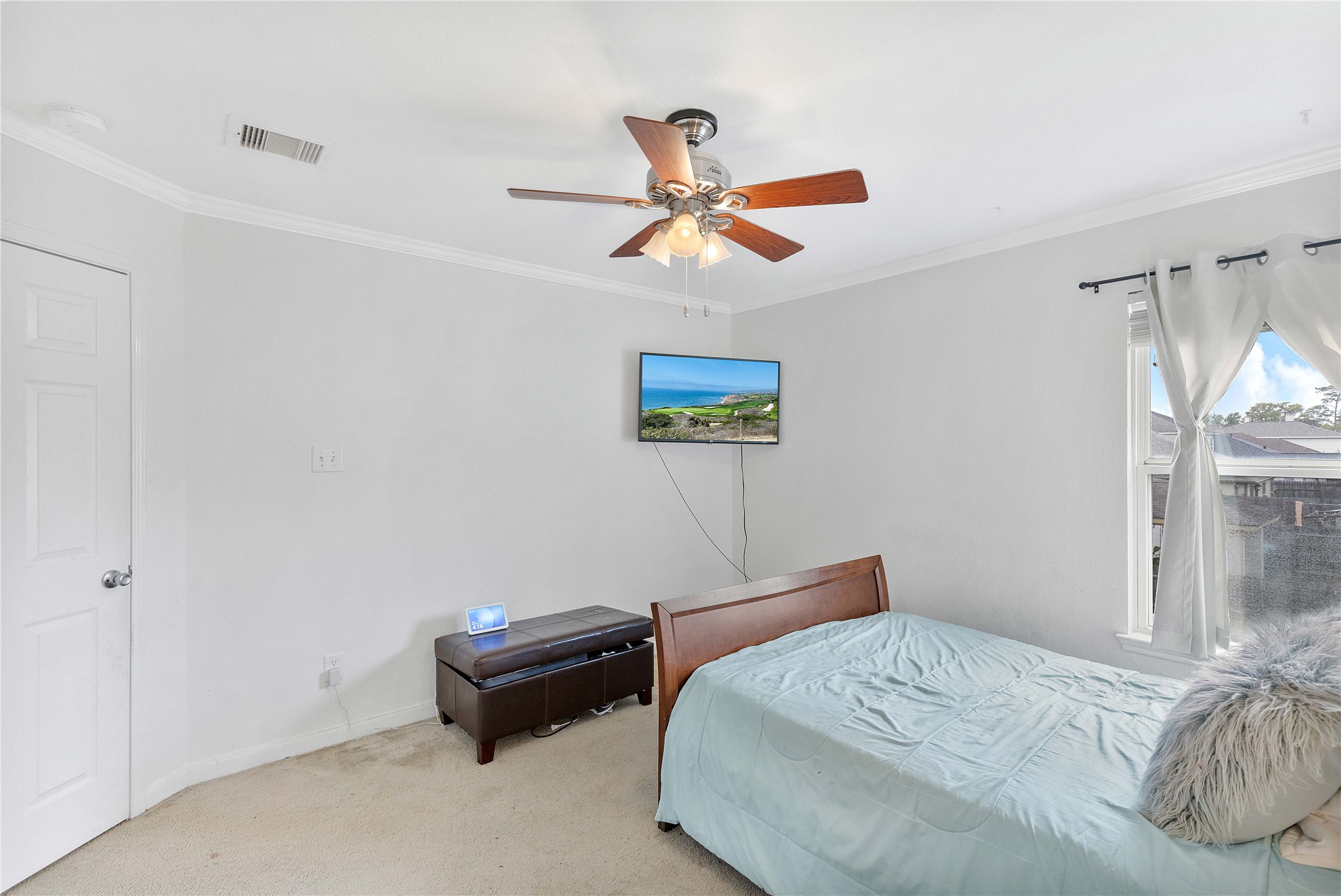 Bright and inviting bedroom featuring a ceiling fan, ample natural light from the window, and a mounted TV, creating a cozy and functional space.