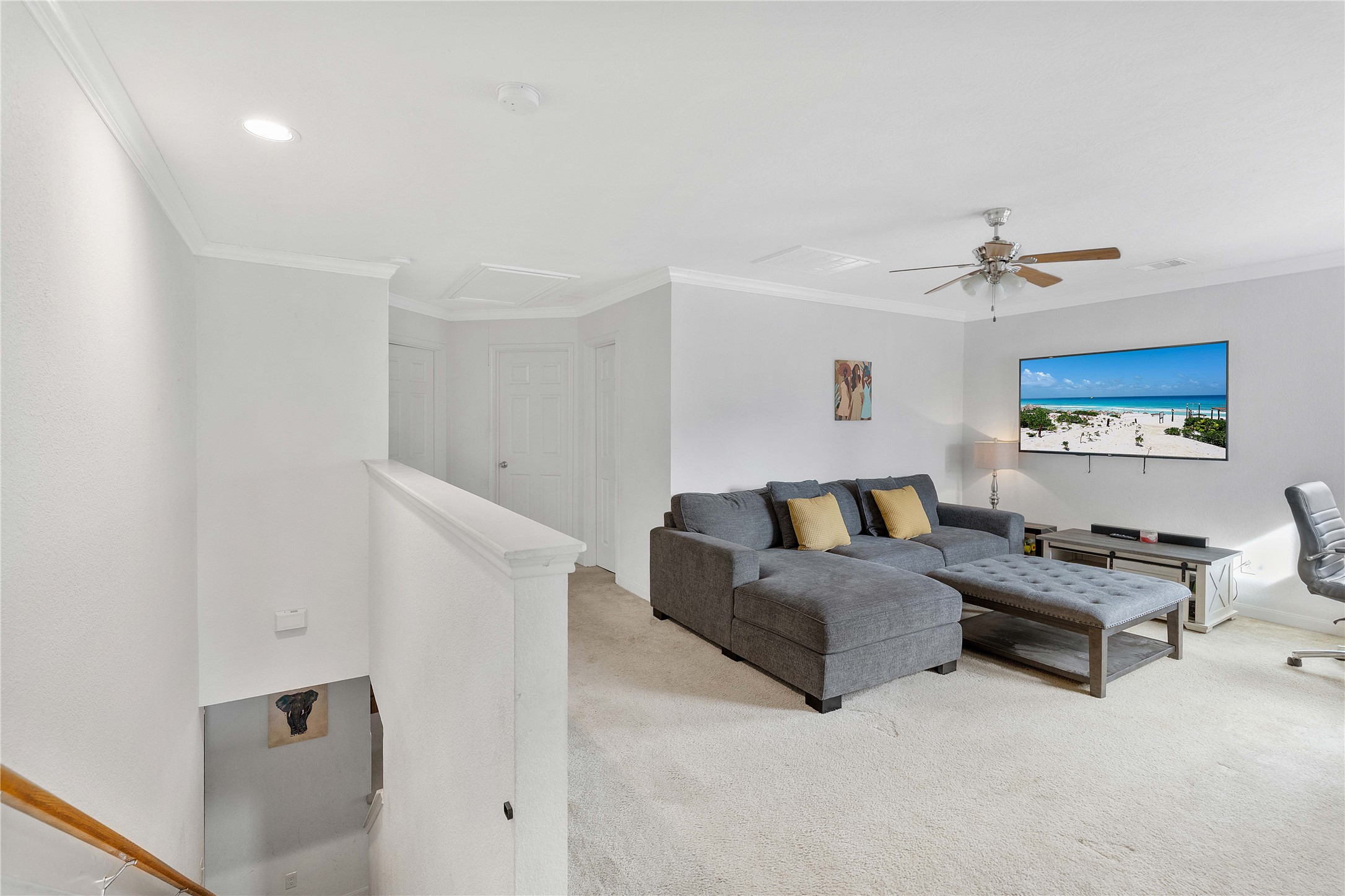Spacious and bright living area featuring a cozy sectional sofa, wall-mounted TV, and ceiling fan, perfect for relaxation.