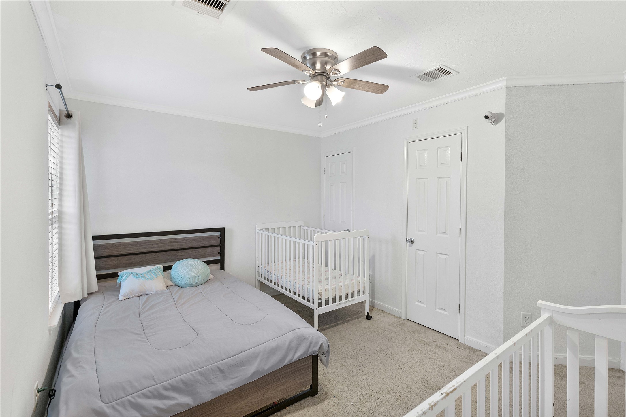 Bright and cozy bedroom featuring a comfortable bed, a crib, soft carpeting, and a ceiling fan for added comfort.
