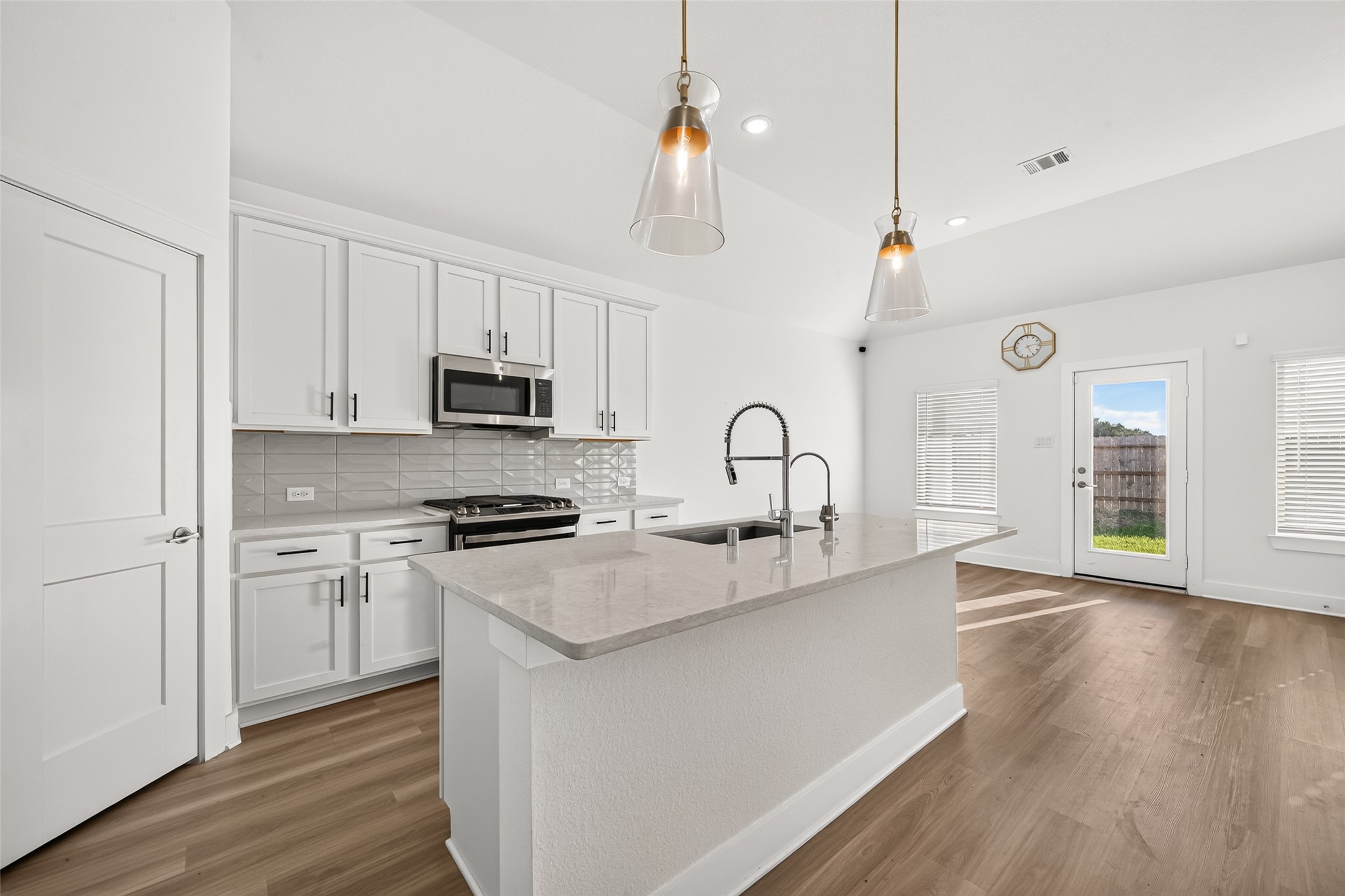 Kitchen island with undermount sink, gooseneck faucet, light countertops, and pendant lighting next to the breakfast area.