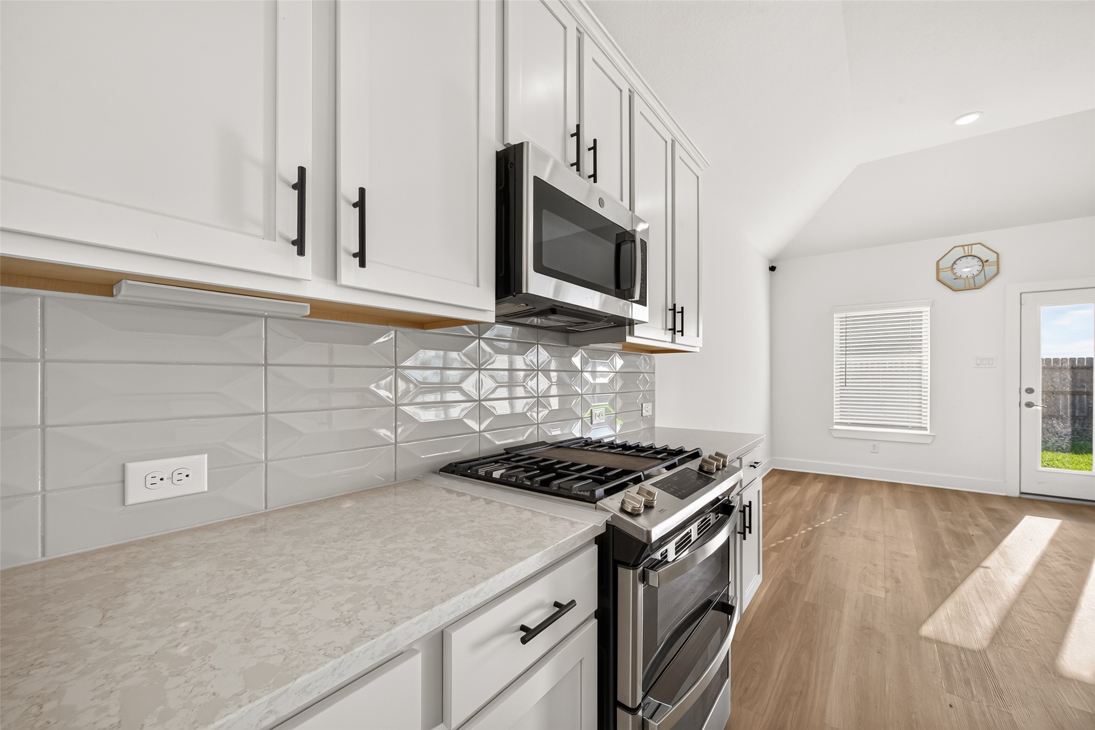 Gas range and stainless steel microwave with white shaker-style cabinets, decorative tile backsplash, and light countertops.